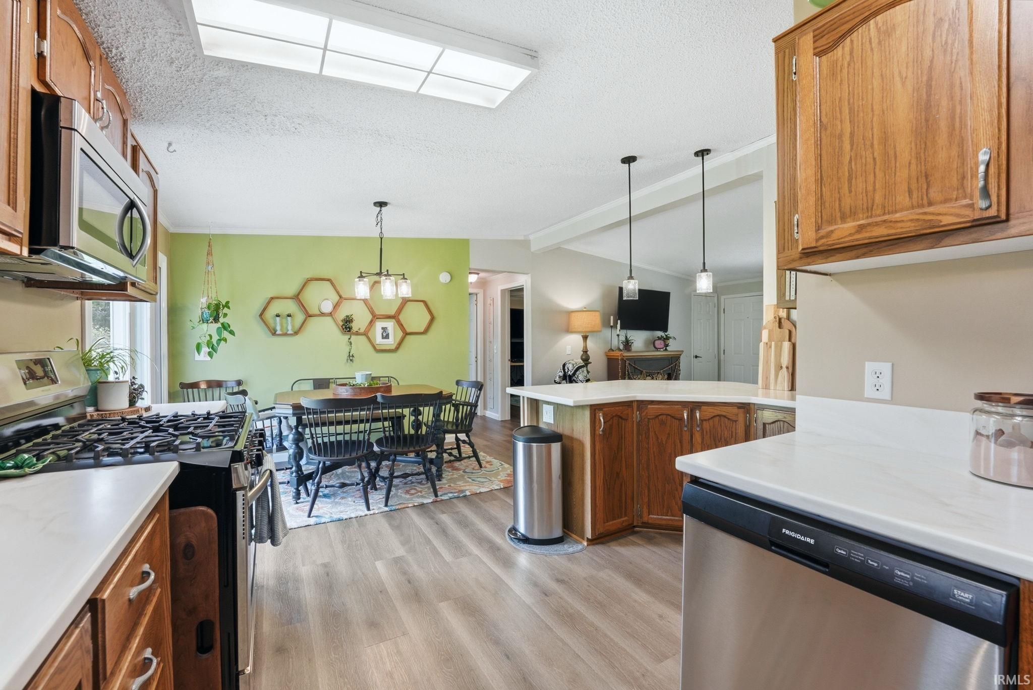 Kitchen with wood finish cabinets, stainless steel appliances, hanging light fixtures, light countertops, and a peninsula