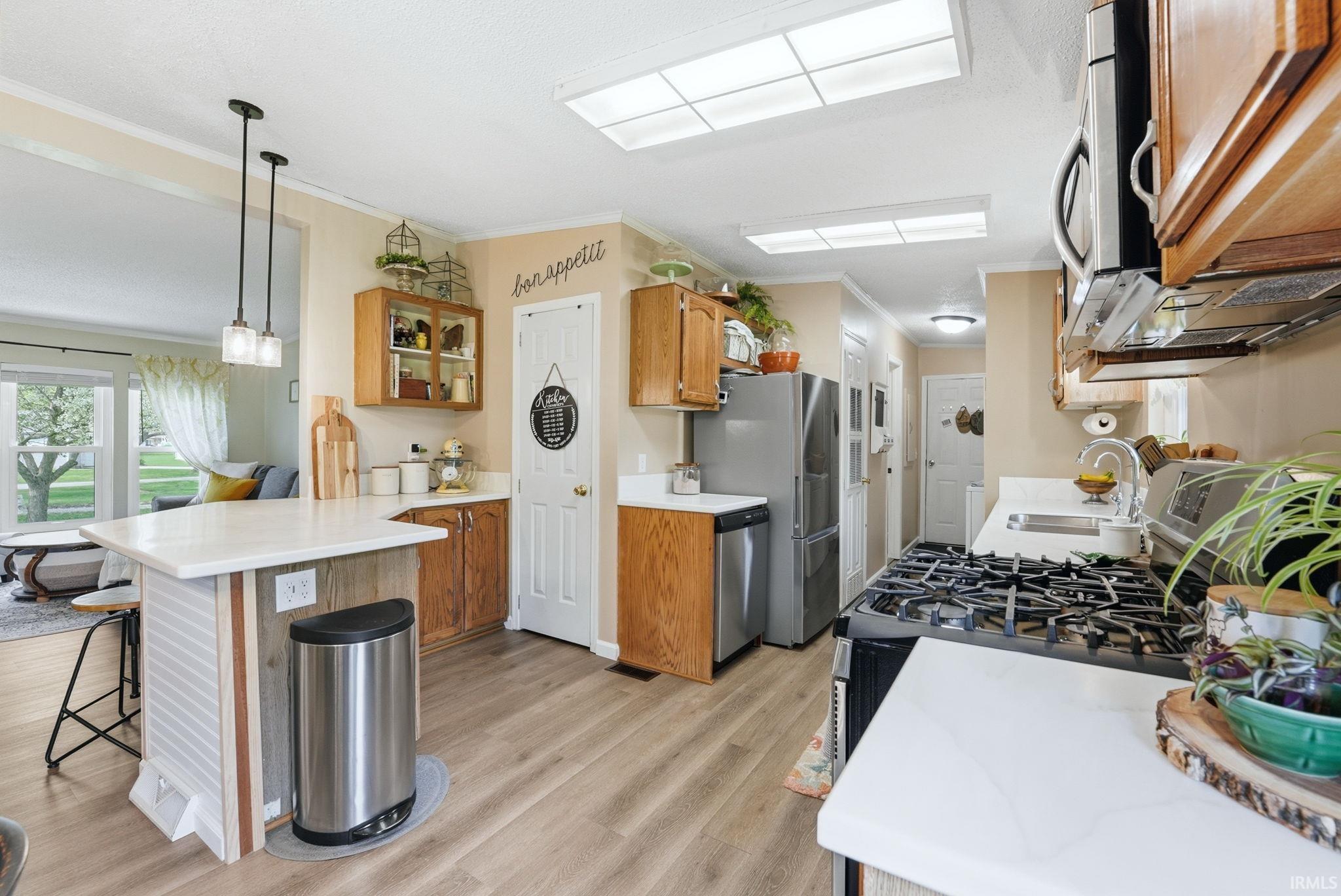 Kitchen featuring wood finish cabinetry, a peninsula, crown molding, light countertops, and a breakfast bar area