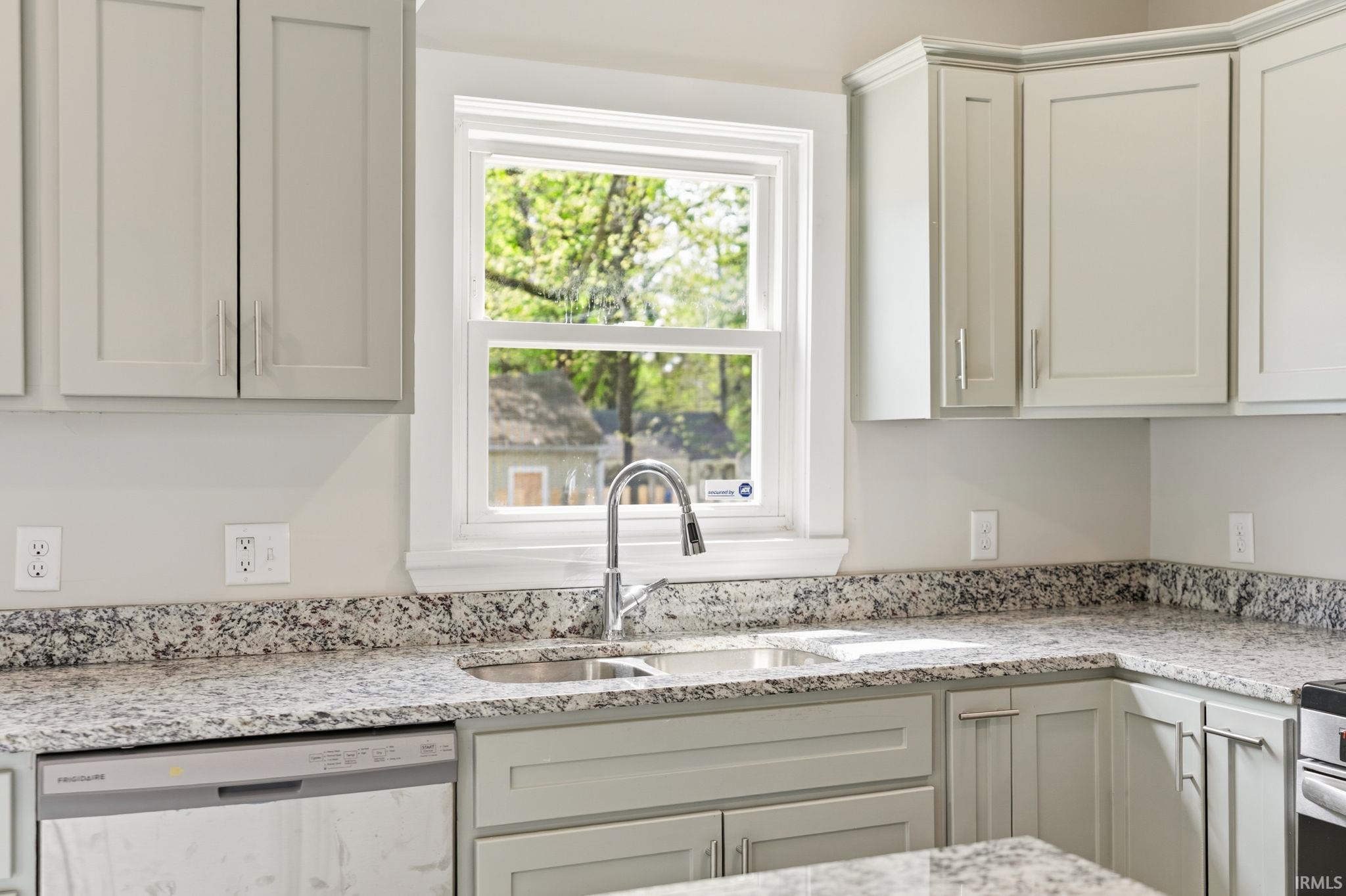 Kitchen with light stone countertops, stainless steel dishwasher, and white cabinets