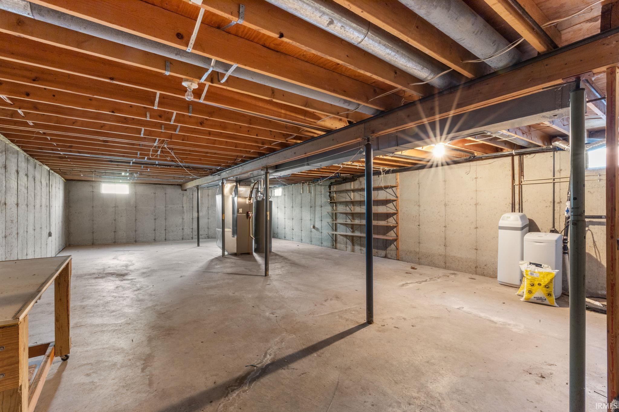Unfinished basement featuring heating unit, a water softener system, and water heater