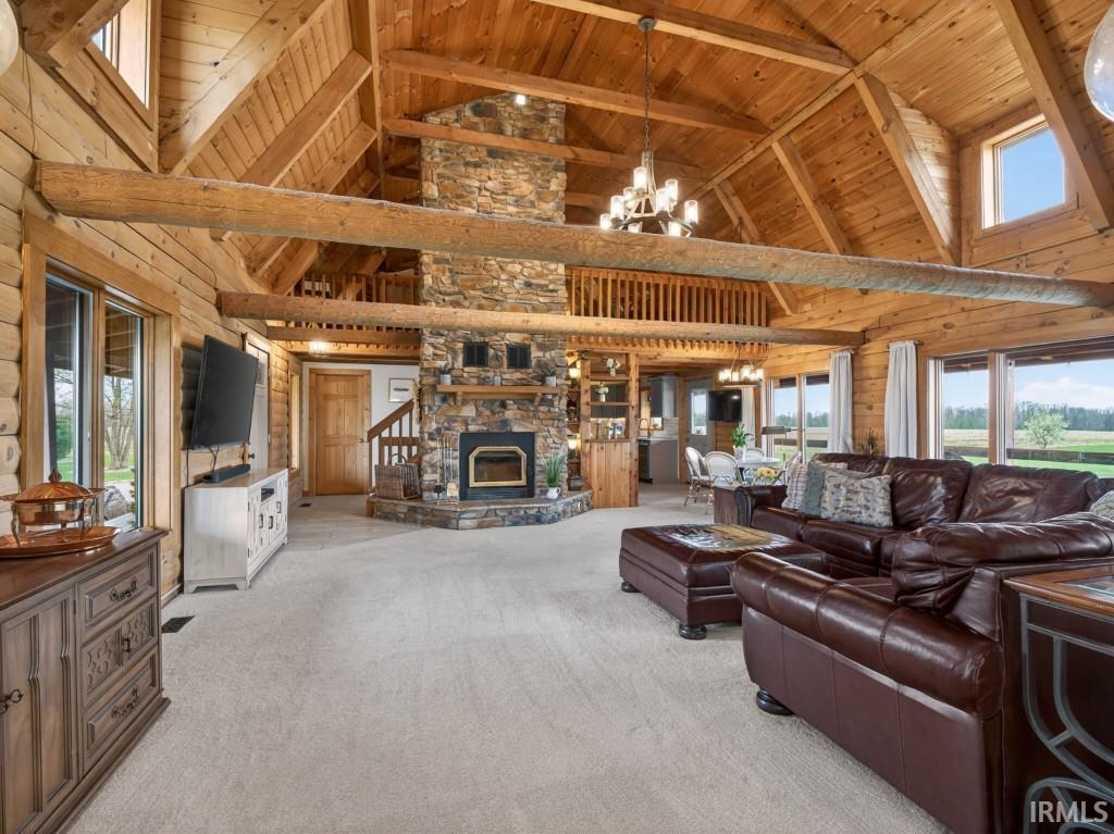 Living room with a chandelier, a high wood beamed ceiling, light colored carpet, wooden walls, and a stone fireplace