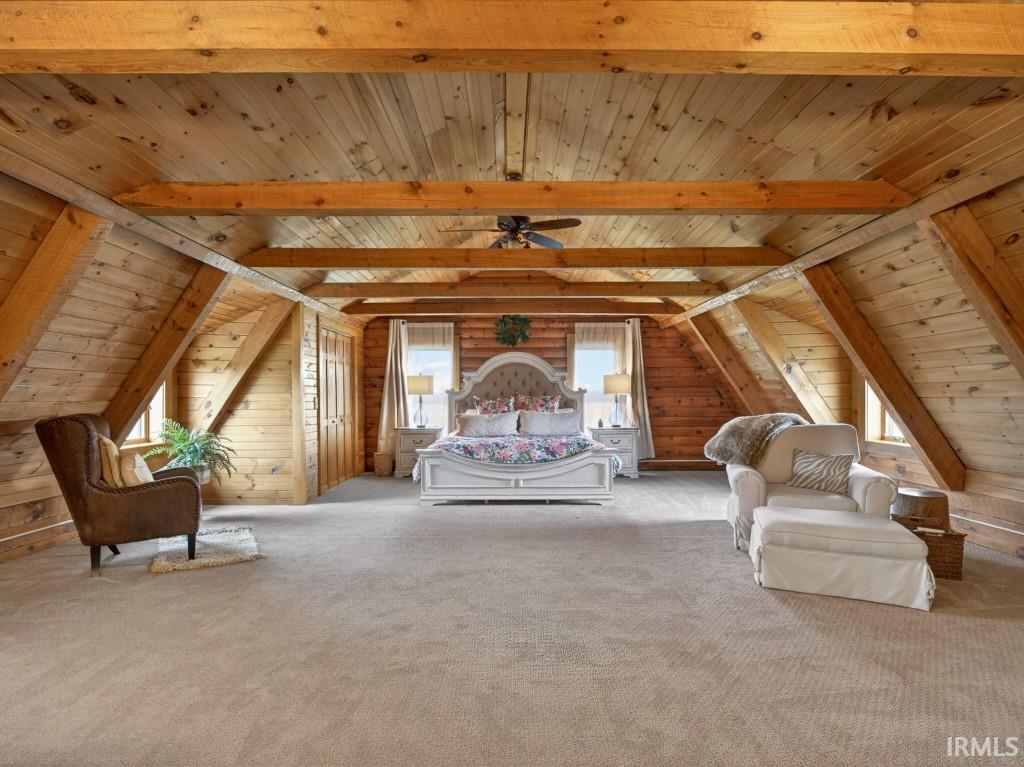 Bedroom featuring multiple windows, a wood ceiling with exposed beams, wood walls, and light colored carpet
