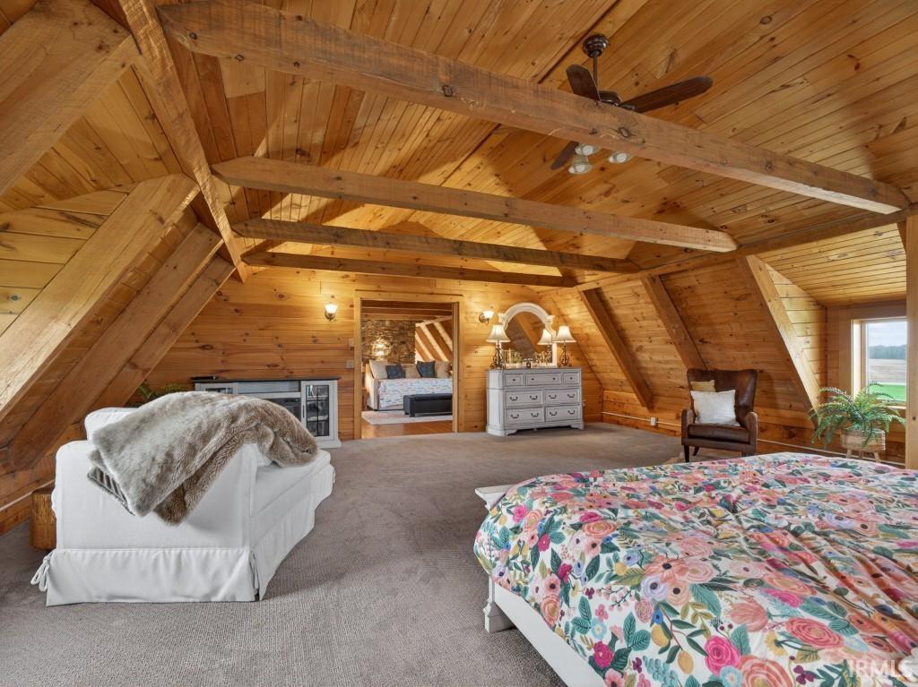 Carpeted bedroom featuring wooden walls and a wooden ceiling with exposed beams
