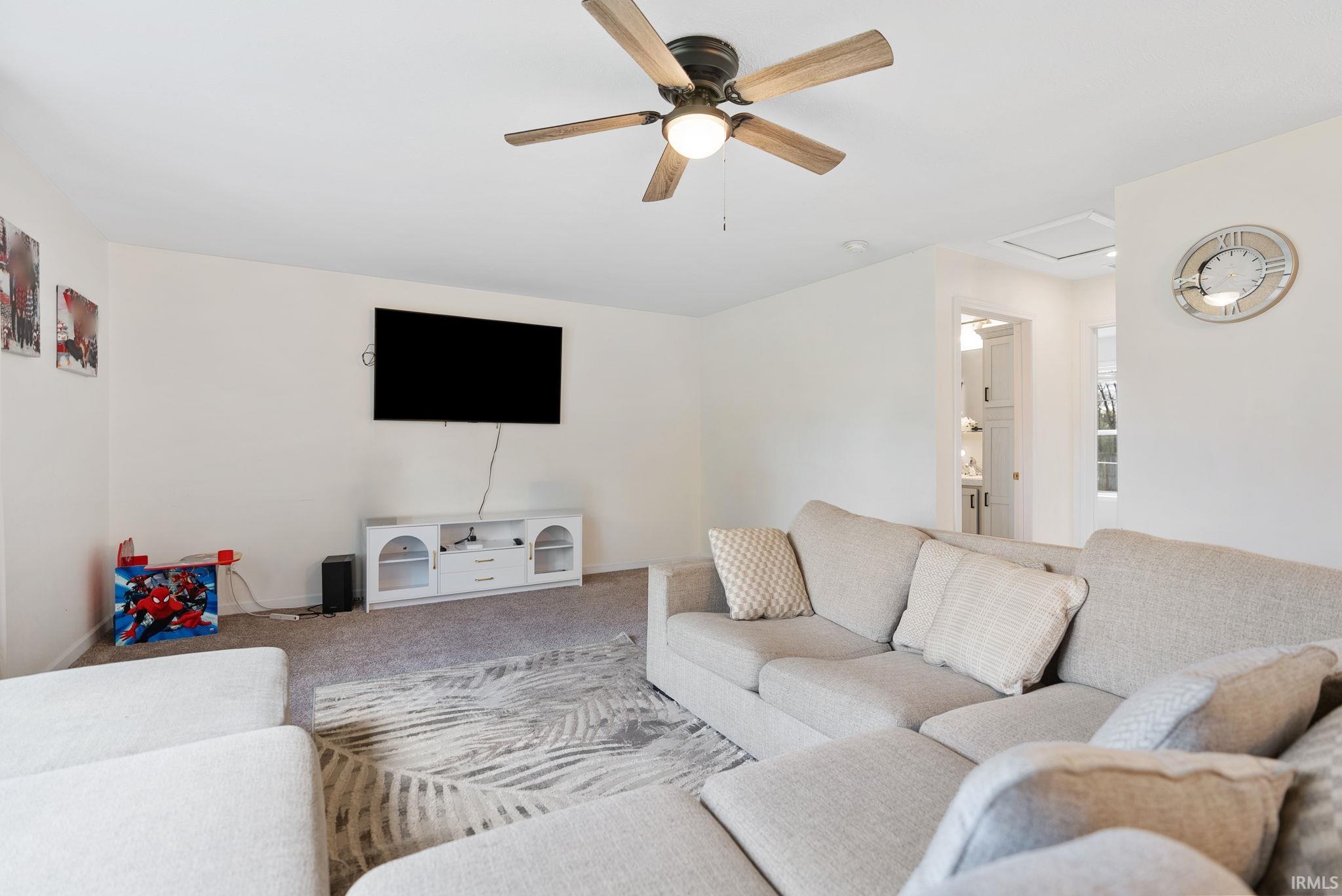 Carpeted living area with a ceiling fan and attic access