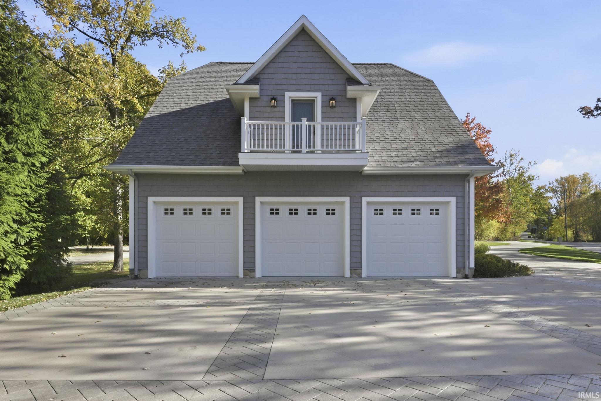 View of property exterior featuring a balcony, a shingled roof, a garage, and driveway