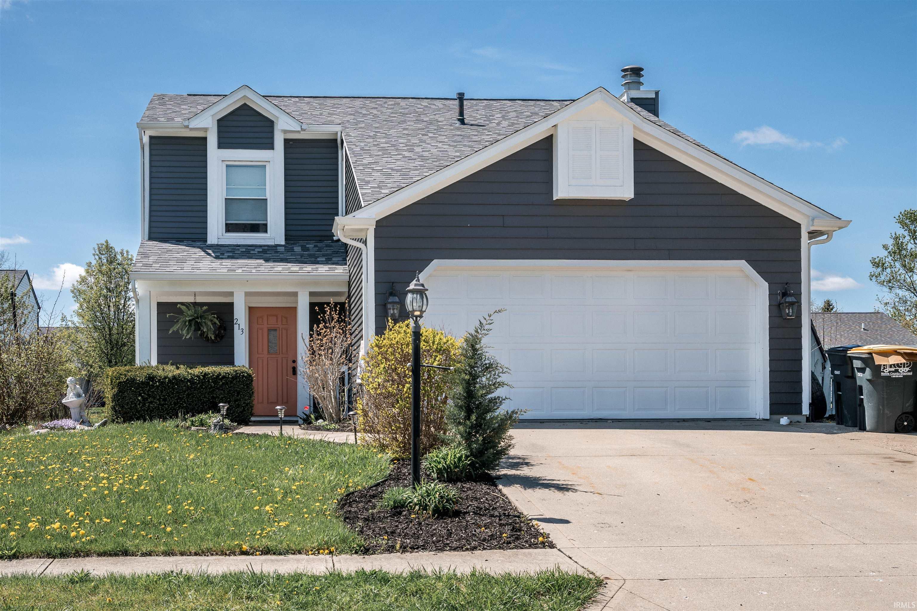 Traditional-style home with driveway, roof with shingles, a front lawn, and a garage