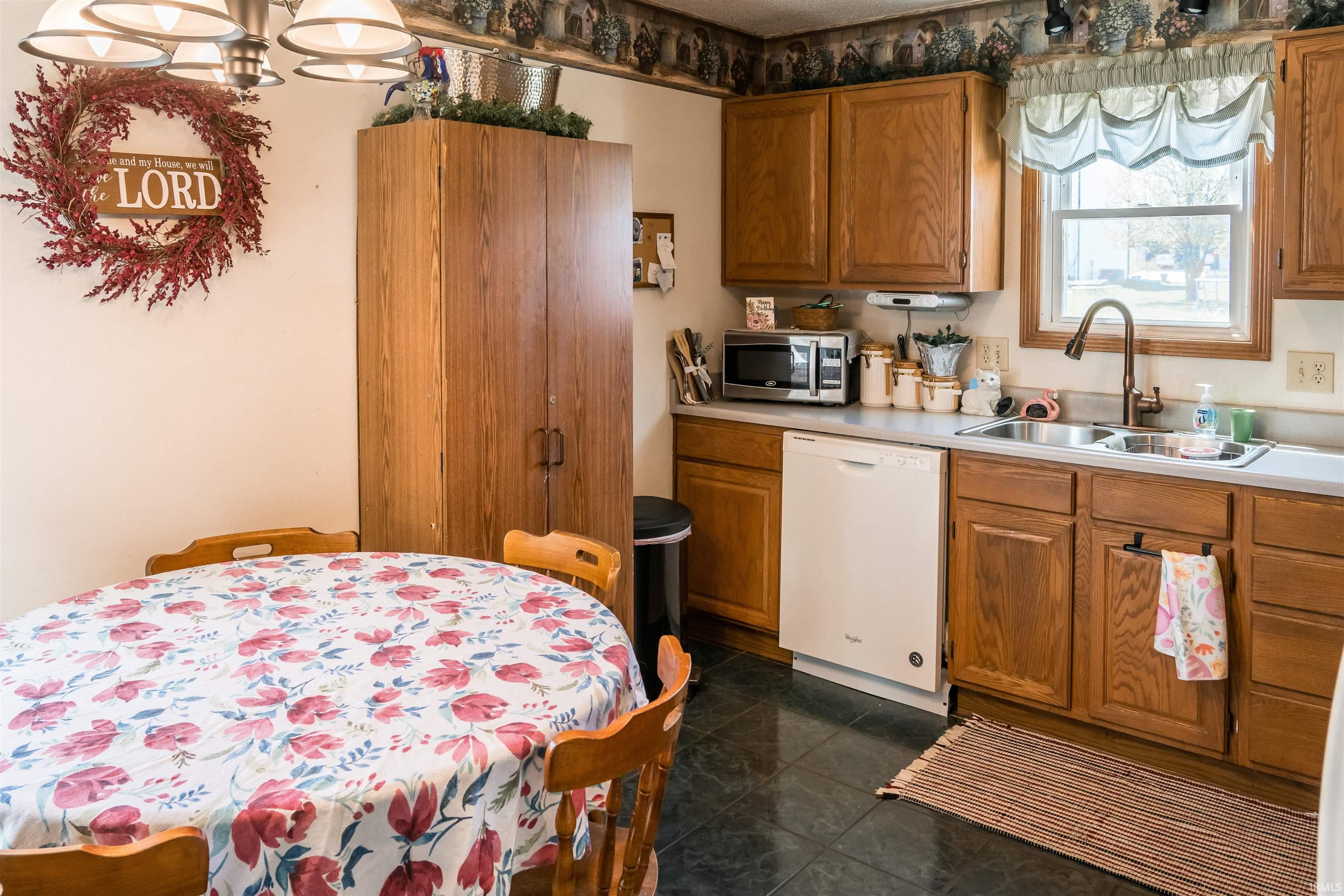 Kitchen with wood finish cabinetry, light countertops, white dishwasher, stainless steel microwave, and a chandelier