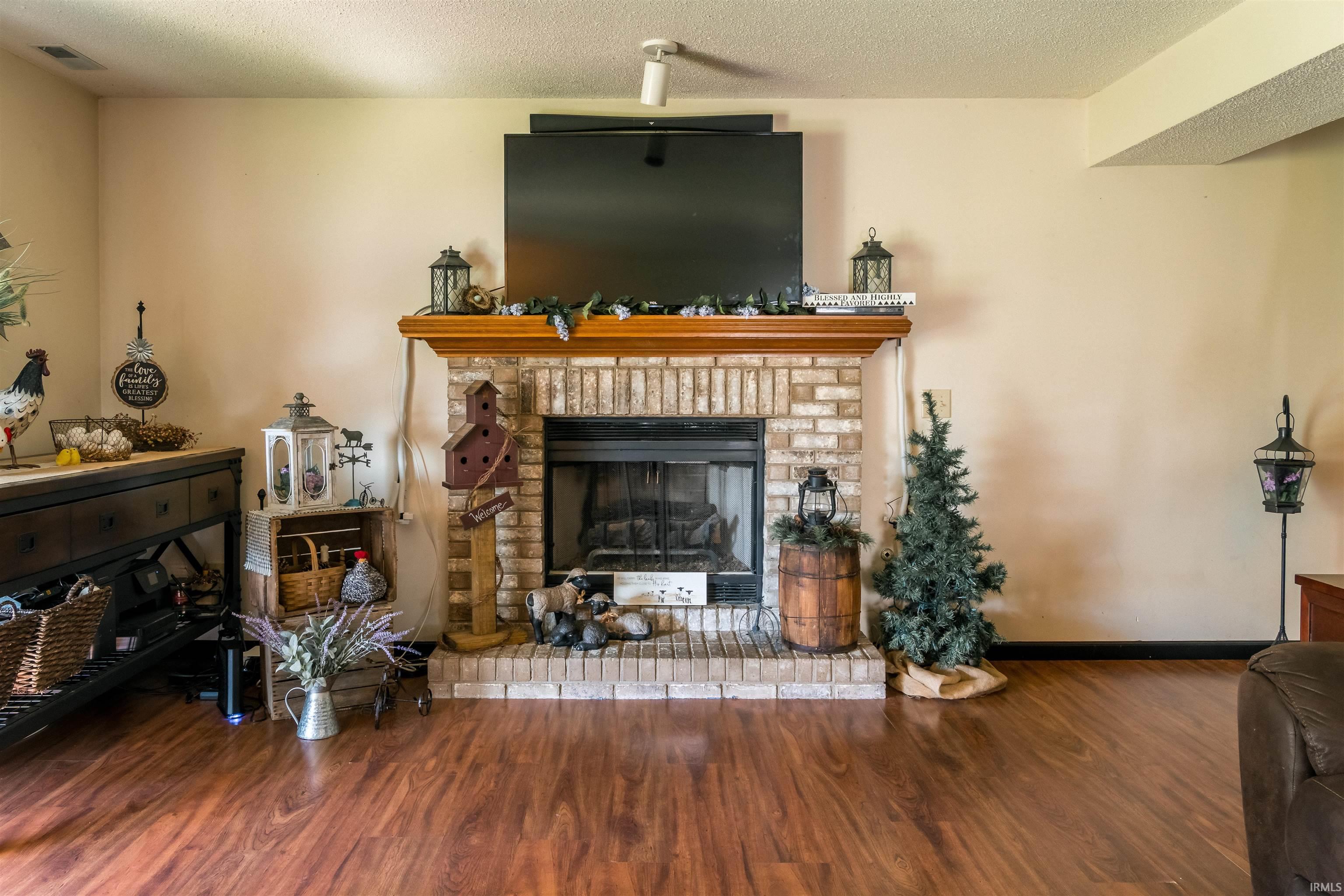 Living area featuring a brick fireplace, wood finished floors, and a textured ceiling