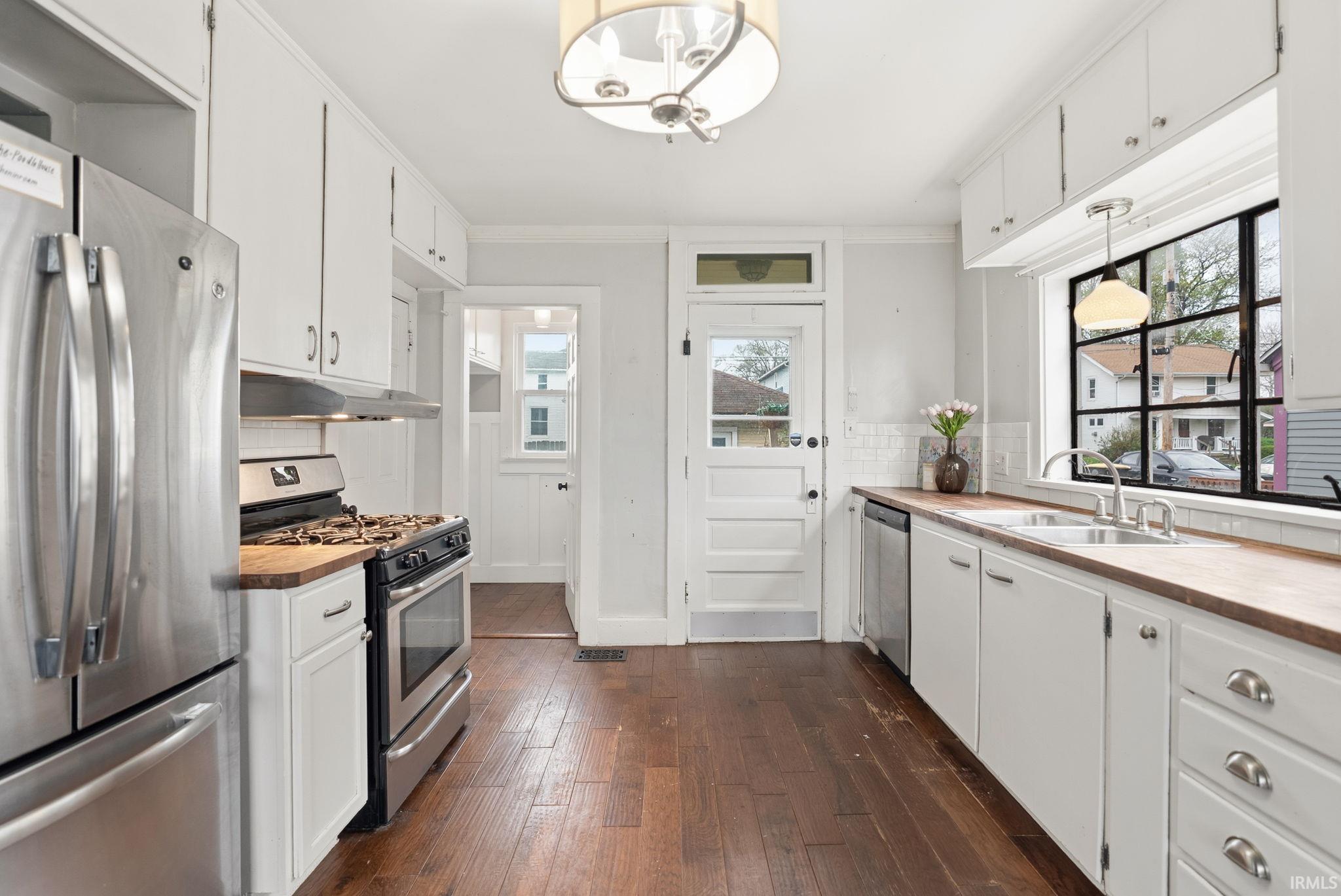 Kitchen featuring stainless steel appliances, white cabinetry, dark wood finished floors, decorative backsplash, and crown molding