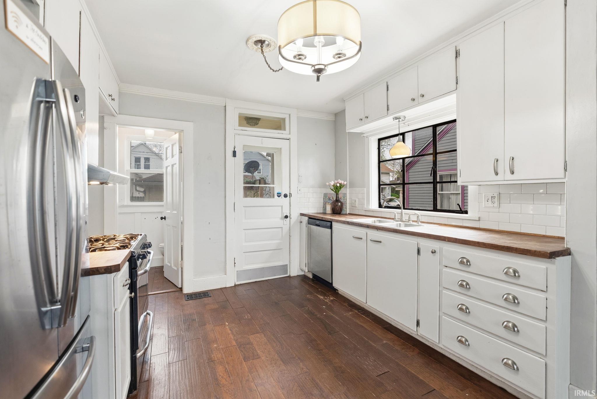 Kitchen with stainless steel appliances, white cabinetry, wooden counters, dark wood-style floors, and crown molding