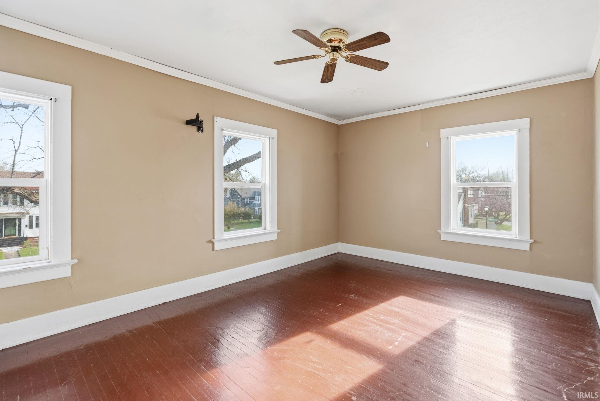 Spare room with wood-type flooring, crown molding, and a ceiling fan