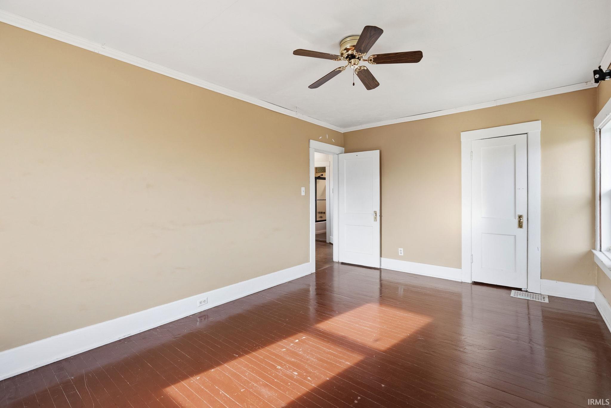 Unfurnished bedroom featuring ornamental molding, dark wood-style flooring, and a ceiling fan