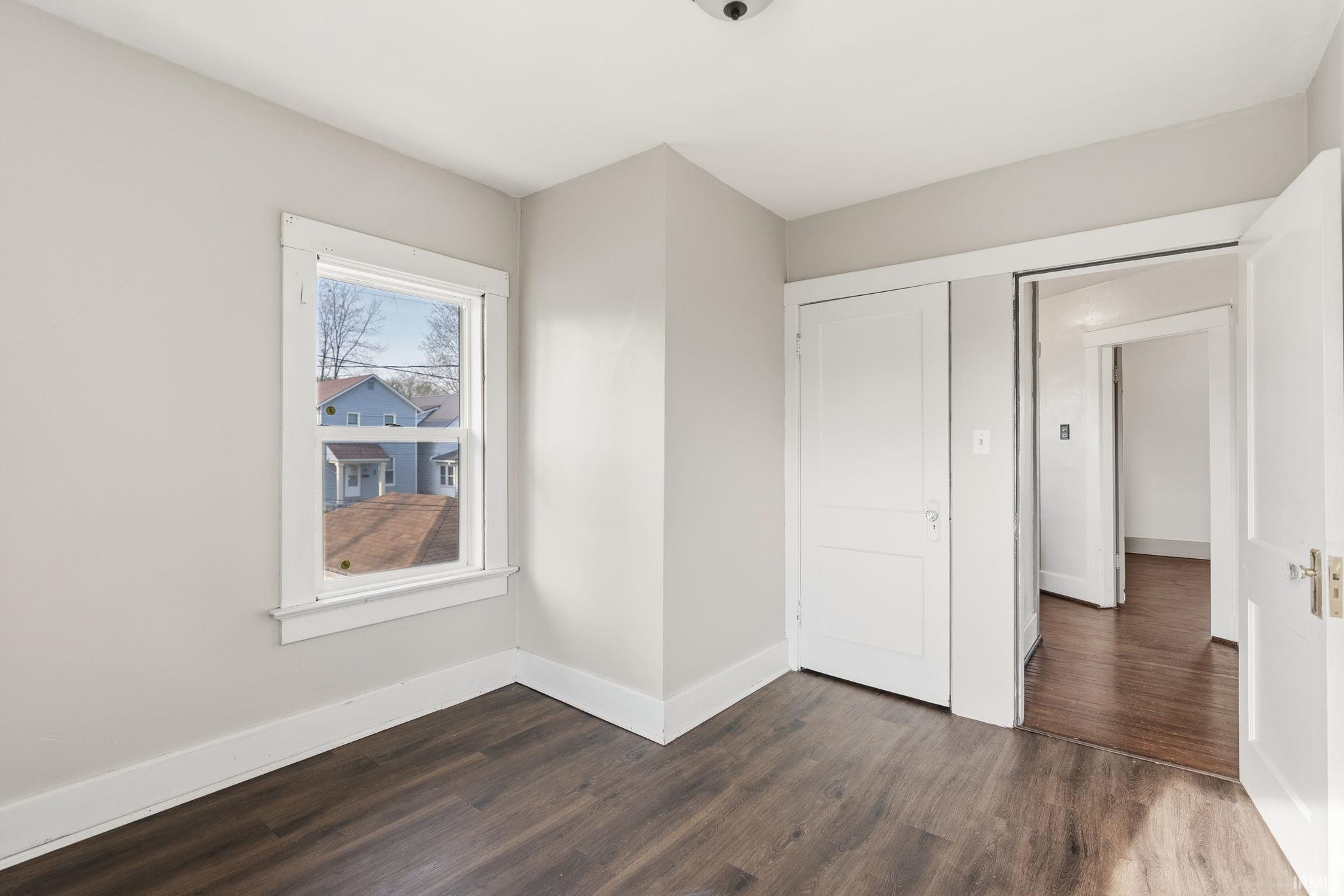 Unfurnished bedroom featuring dark wood-style flooring and baseboards