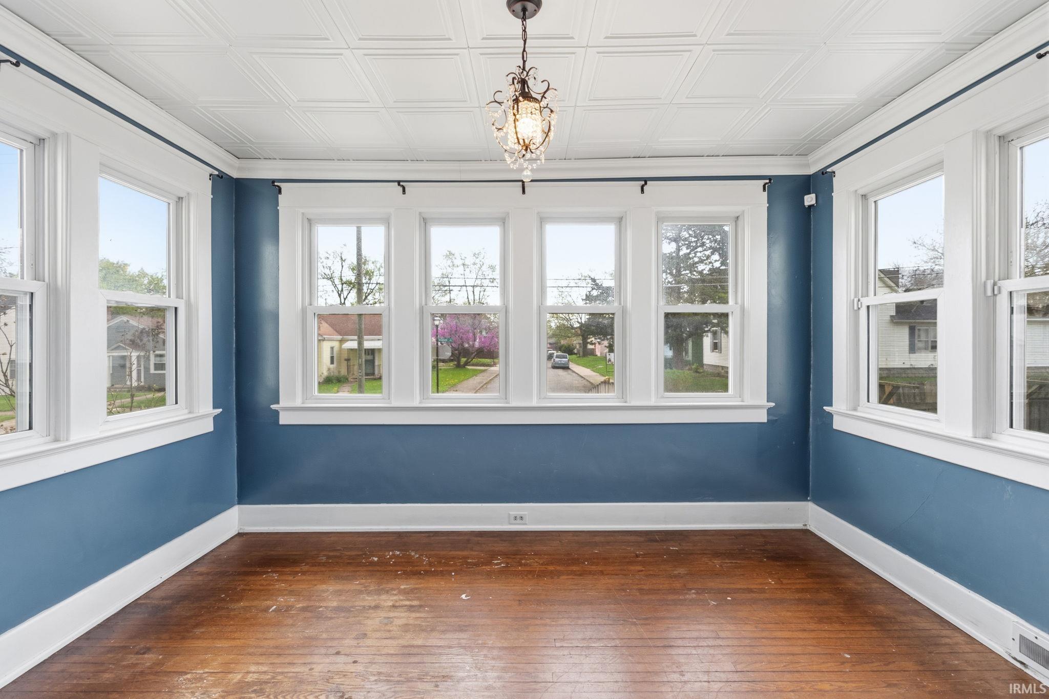 Unfurnished sunroom featuring wood-type flooring, plenty of natural light, and a chandelier