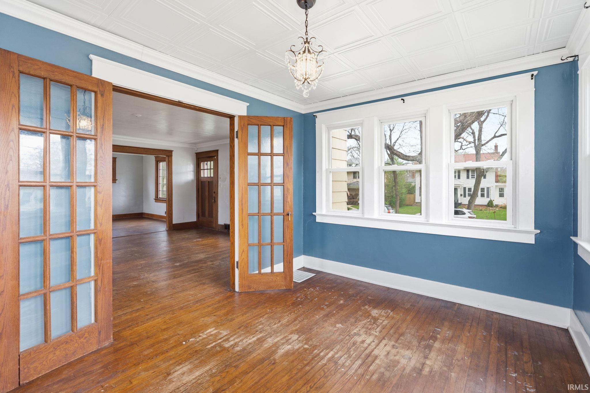 Spare room featuring dark wood finished floors, hanging lights, french doors, and an ornate ceiling