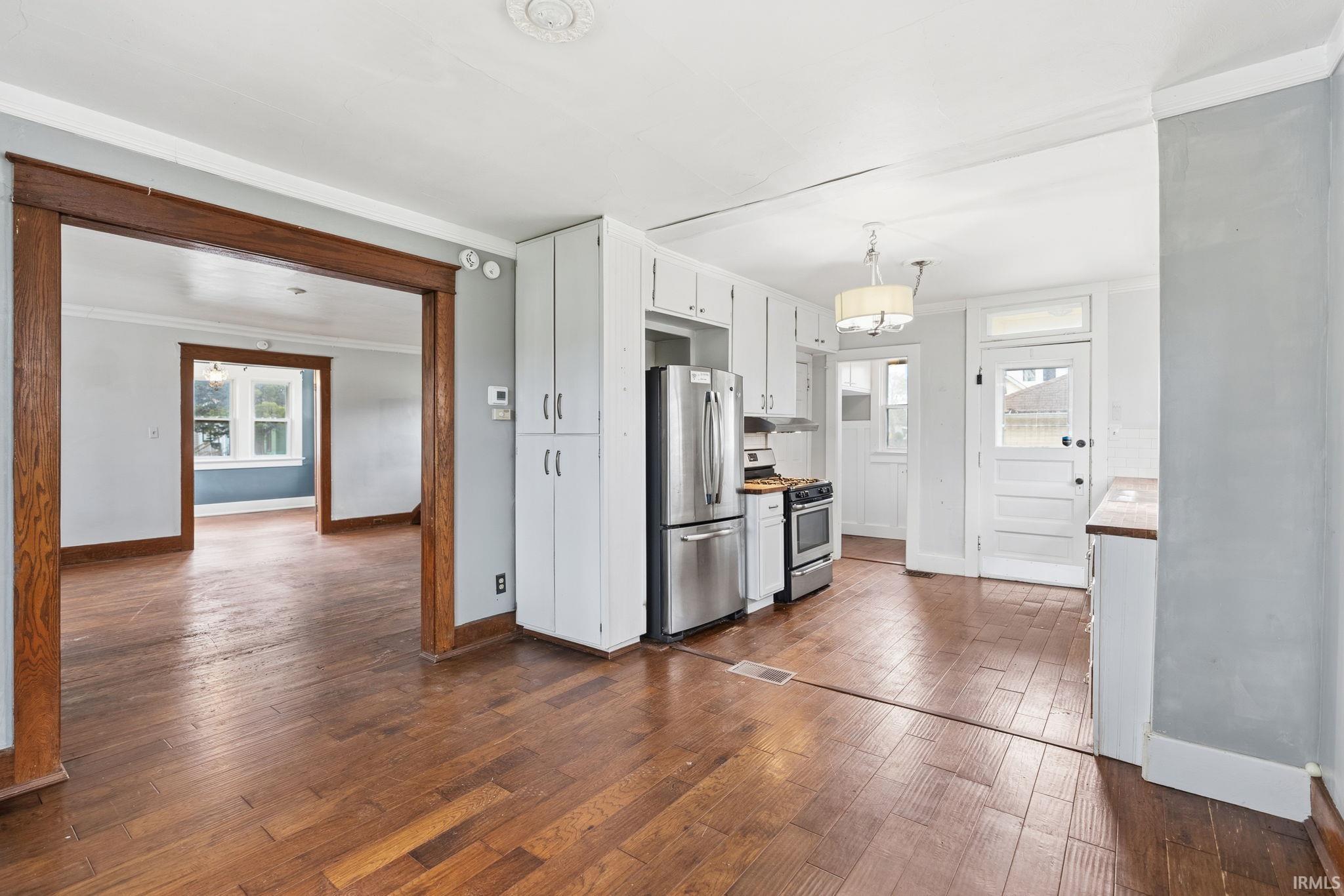 Kitchen with crown molding, white cabinets, dark wood-style flooring, stainless steel appliances, and decorative light fixtures