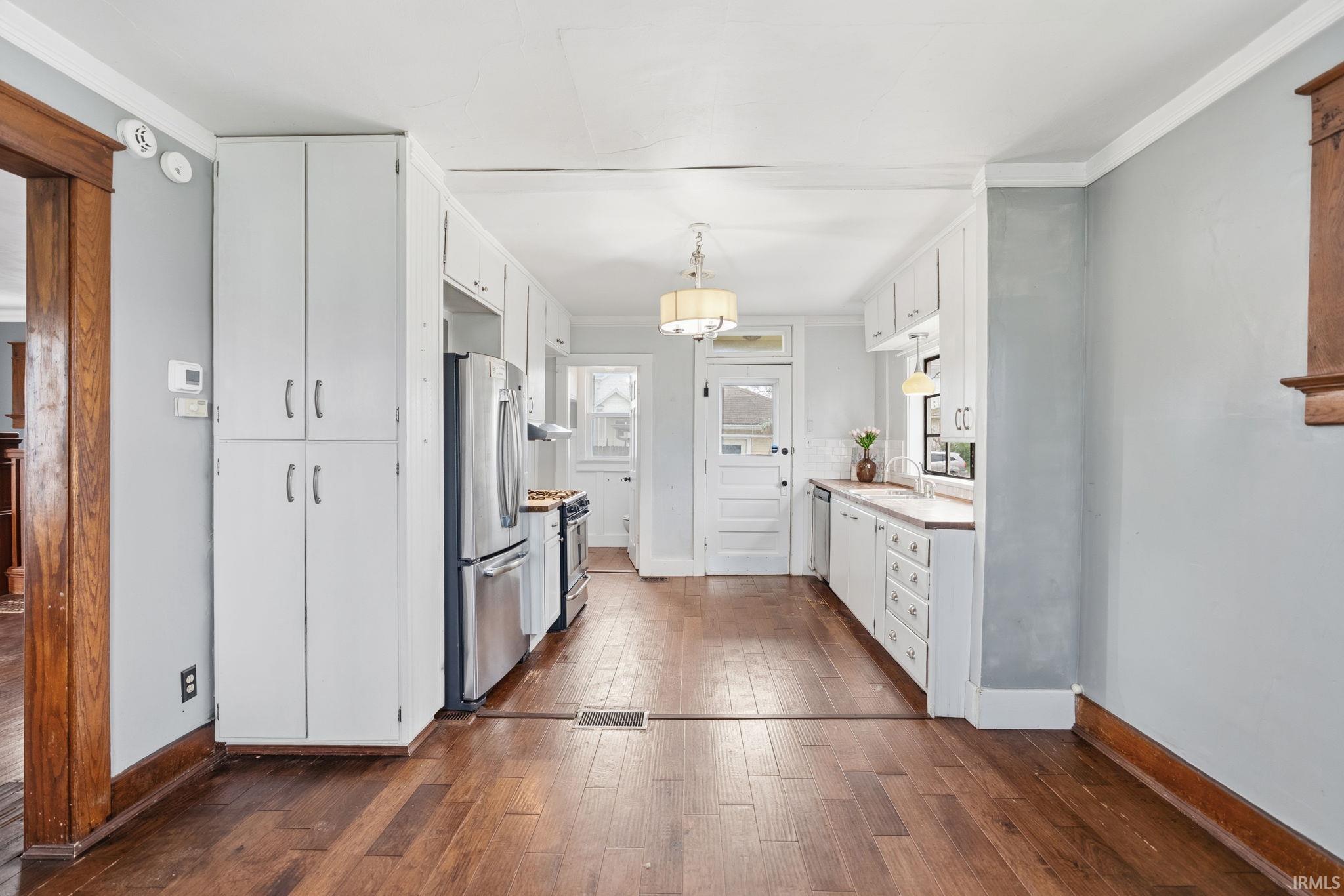Kitchen with white cabinetry, dark wood finished floors, ornamental molding, stainless steel appliances, and light countertops