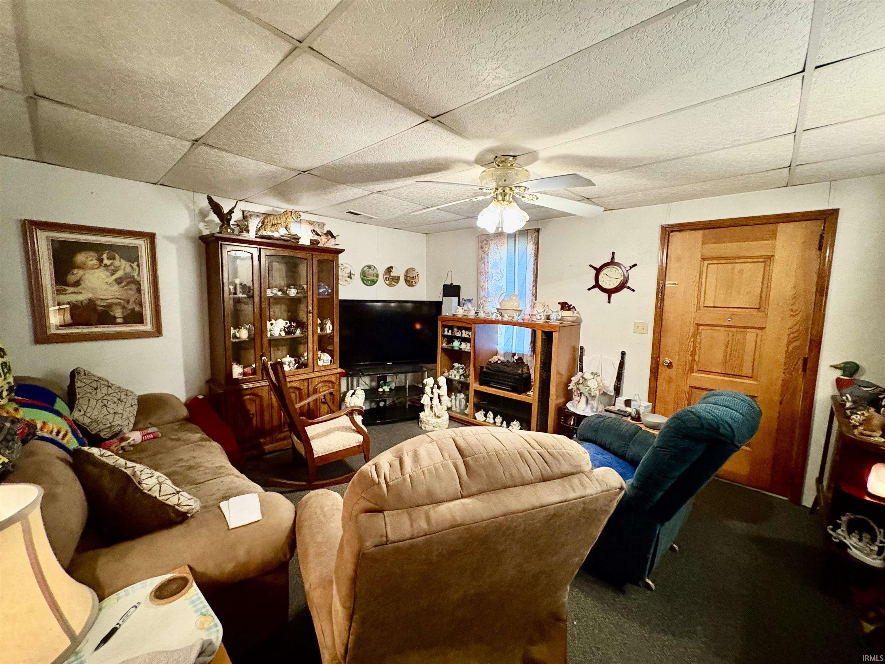 Living room featuring carpet flooring, ceiling fan, and a paneled ceiling