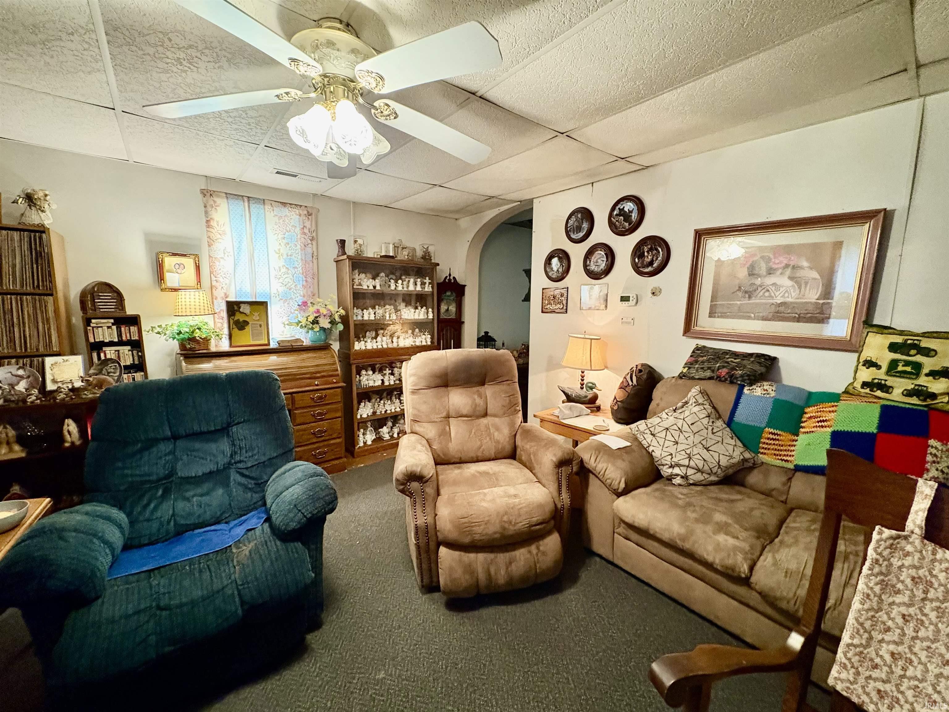 Sitting room featuring carpet floors, arched walkways, a drop ceiling, and a ceiling fan