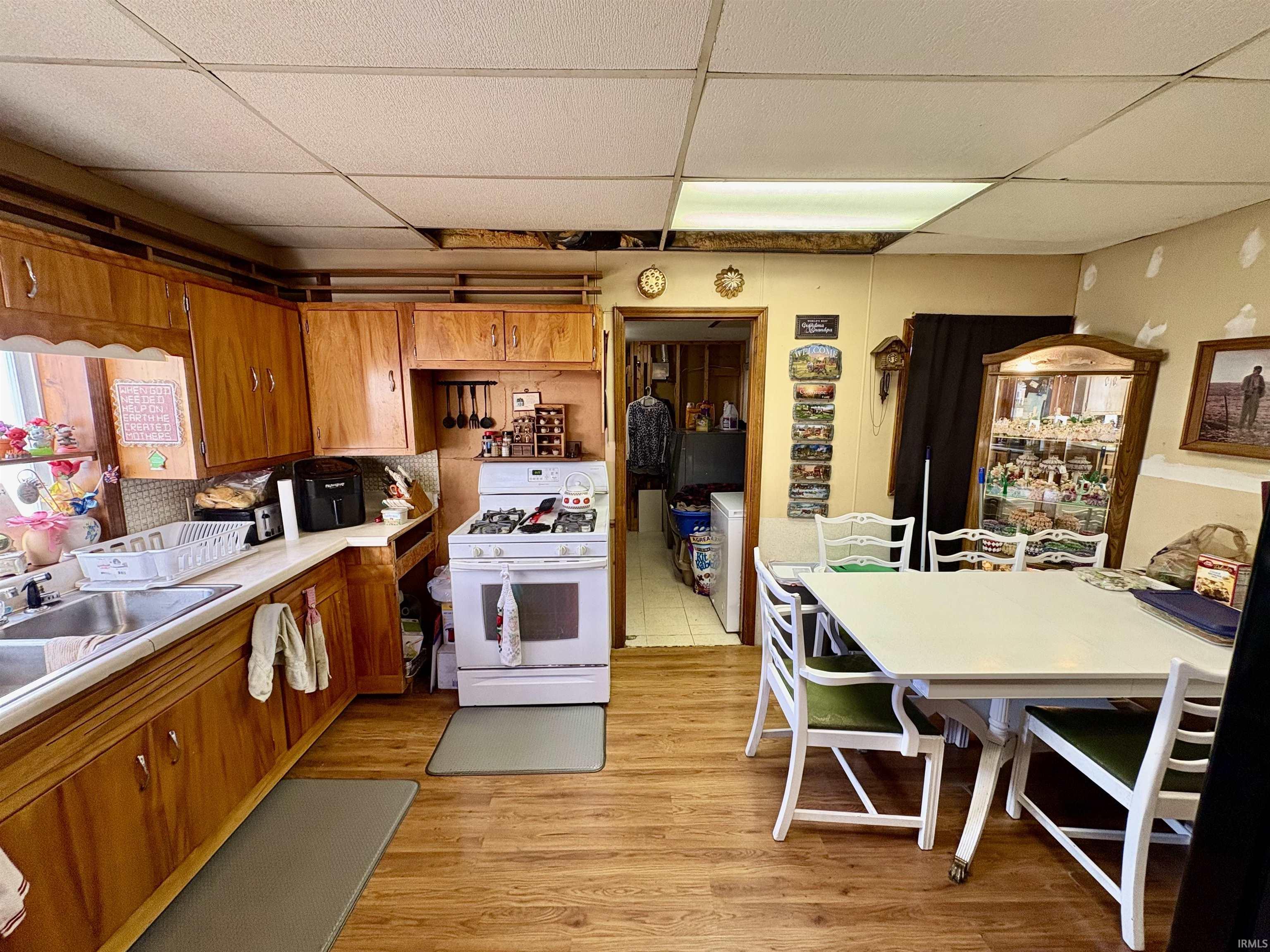 Kitchen featuring brown cabinets, a paneled ceiling, light countertops, white gas range oven, and light wood-style flooring