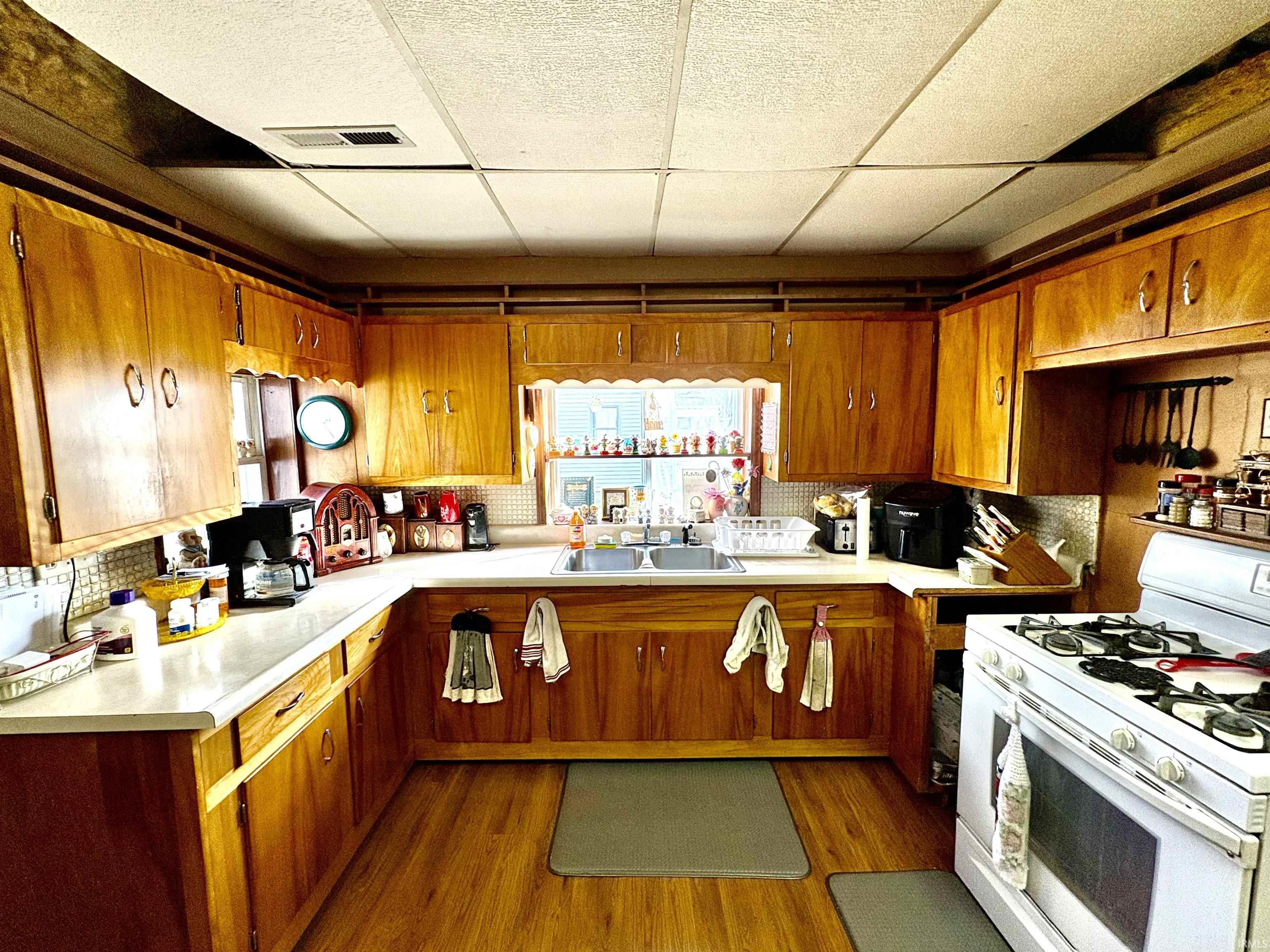 Kitchen featuring a paneled ceiling, gas range gas stove, light countertops, decorative backsplash, and brown cabinets