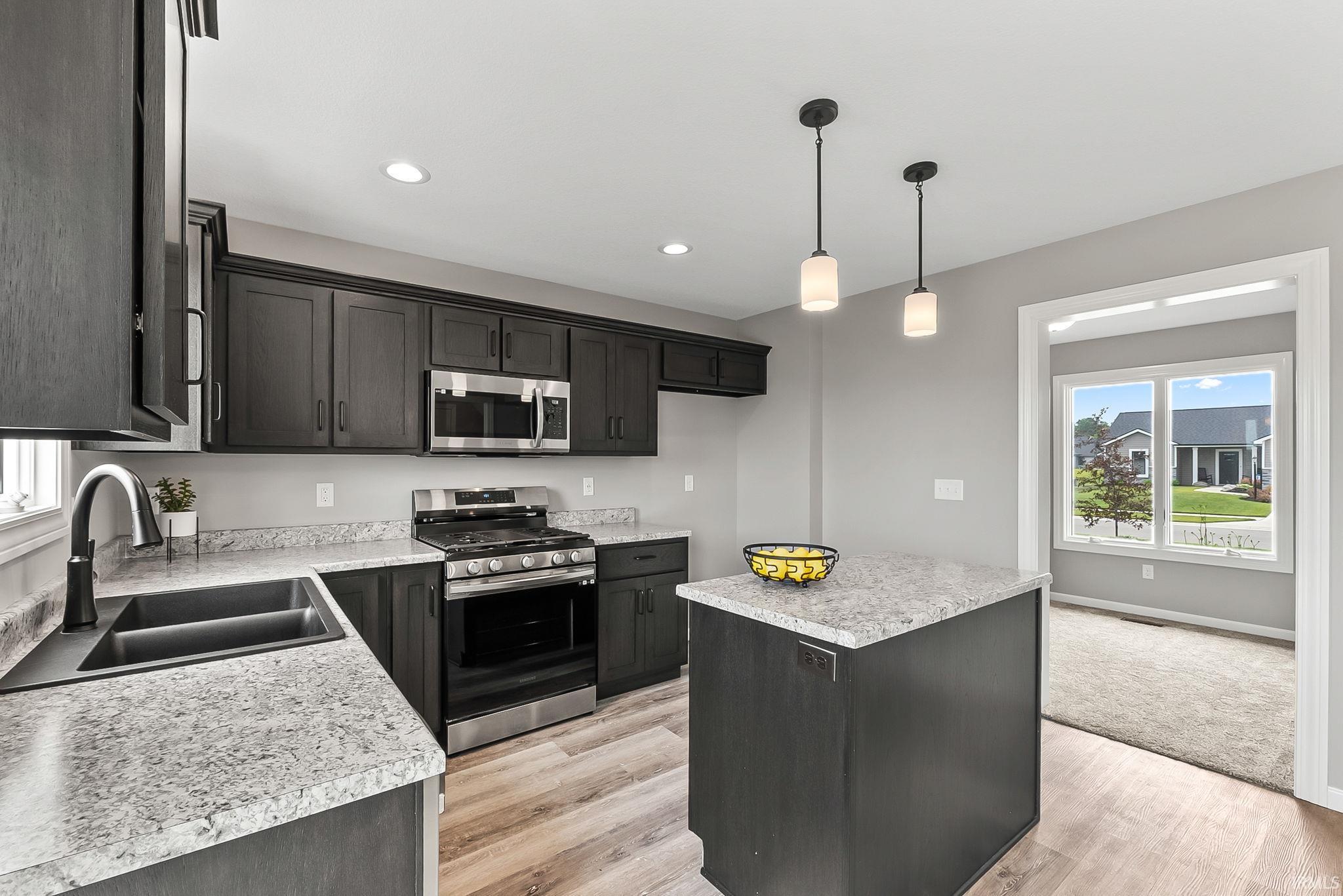 Contemporary kitchen featuring dark wood-finish cabinetry, light speckled countertops, stainless steel appliances, and wood-finish flooring