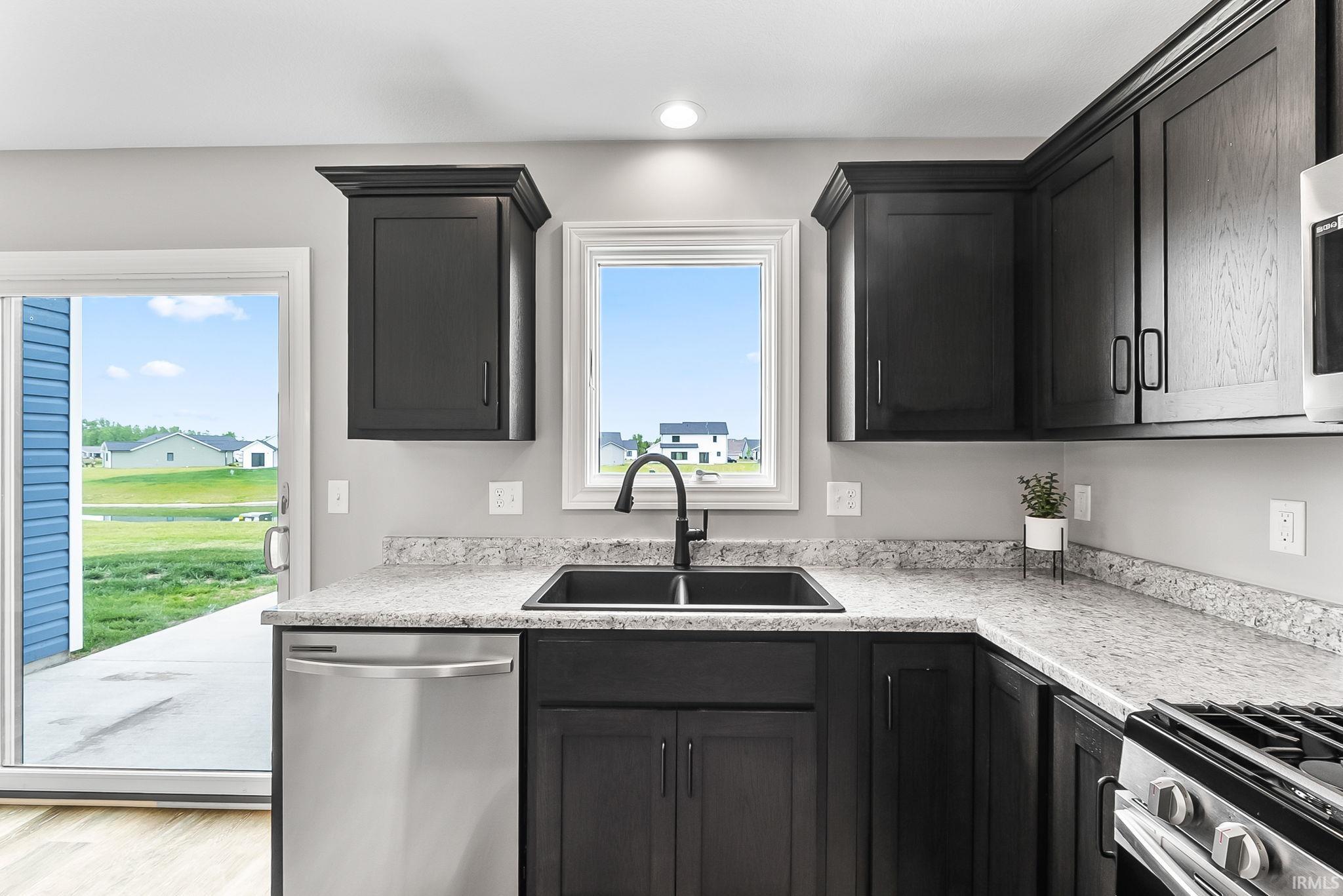 Kitchen featuring dark wood cabinetry, light-toned countertops, stainless steel dishwasher, black sink with a matte black faucet, and light wood-finish flooring