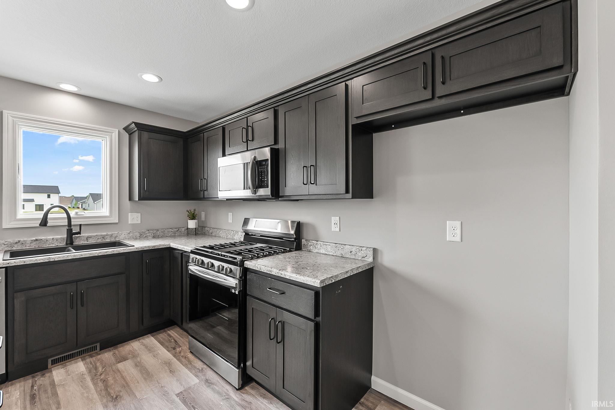 Modern kitchen featuring dark wood-finish cabinetry, light-toned countertops, wood-finish flooring, a stainless steel gas range, and a stainless steel microwave