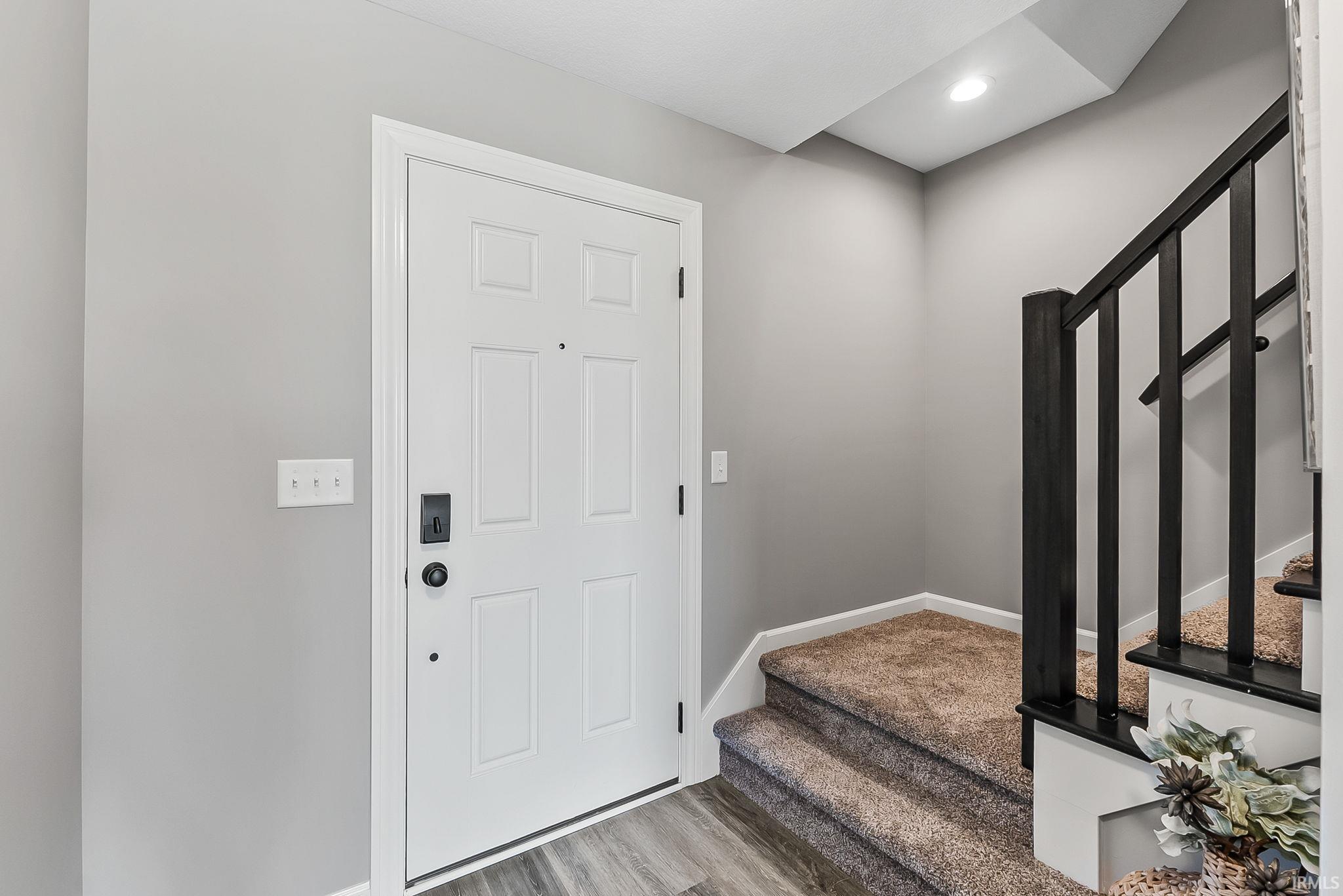 Entryway featuring a paneled door with contemporary hardware, wood-finish flooring, and a carpeted staircase with a black baluster railing