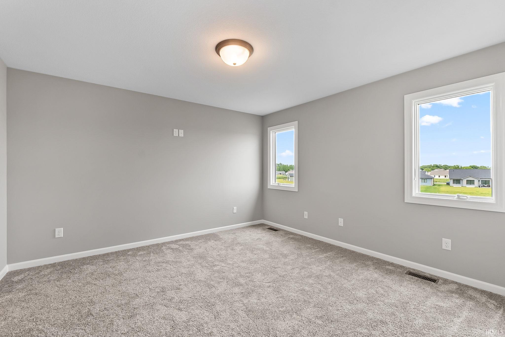 Spacious room featuring neutral gray walls, light gray carpeting, and two bright windows with white trim