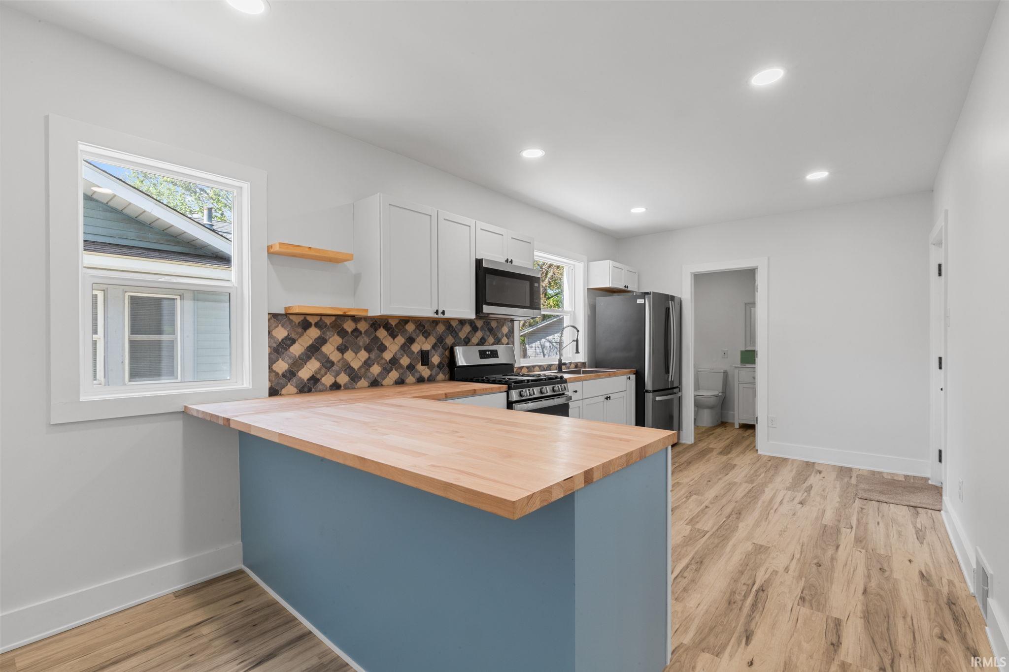 Kitchen featuring a peninsula, open shelves, backsplash, butcher block counters, and stainless steel appliances