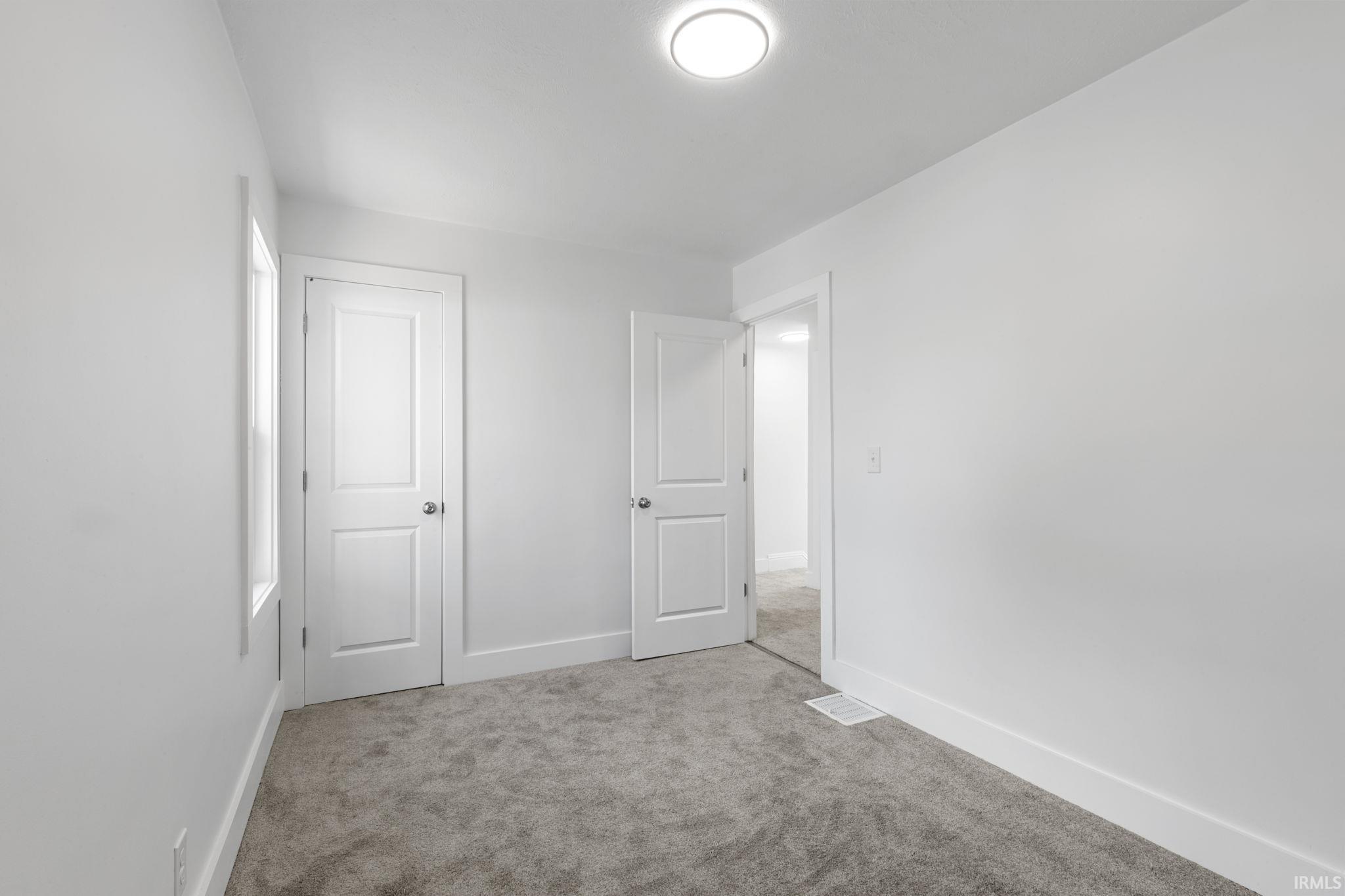 Unfurnished bedroom with light carpet and baseboards