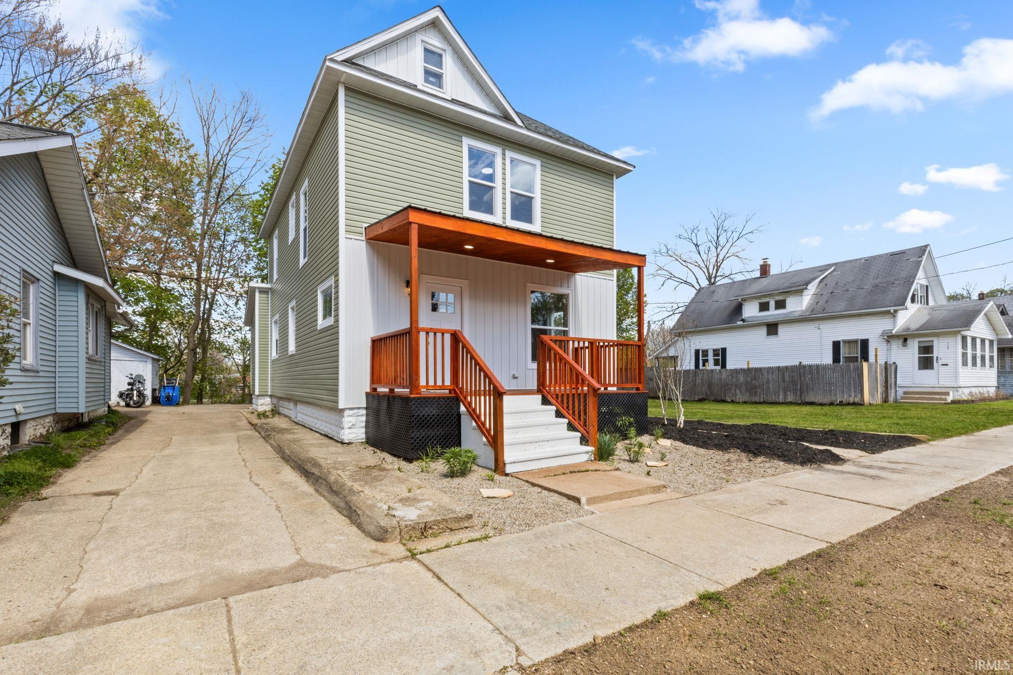 American foursquare style home with a porch, a front lawn, board and batten siding, and a detached garage