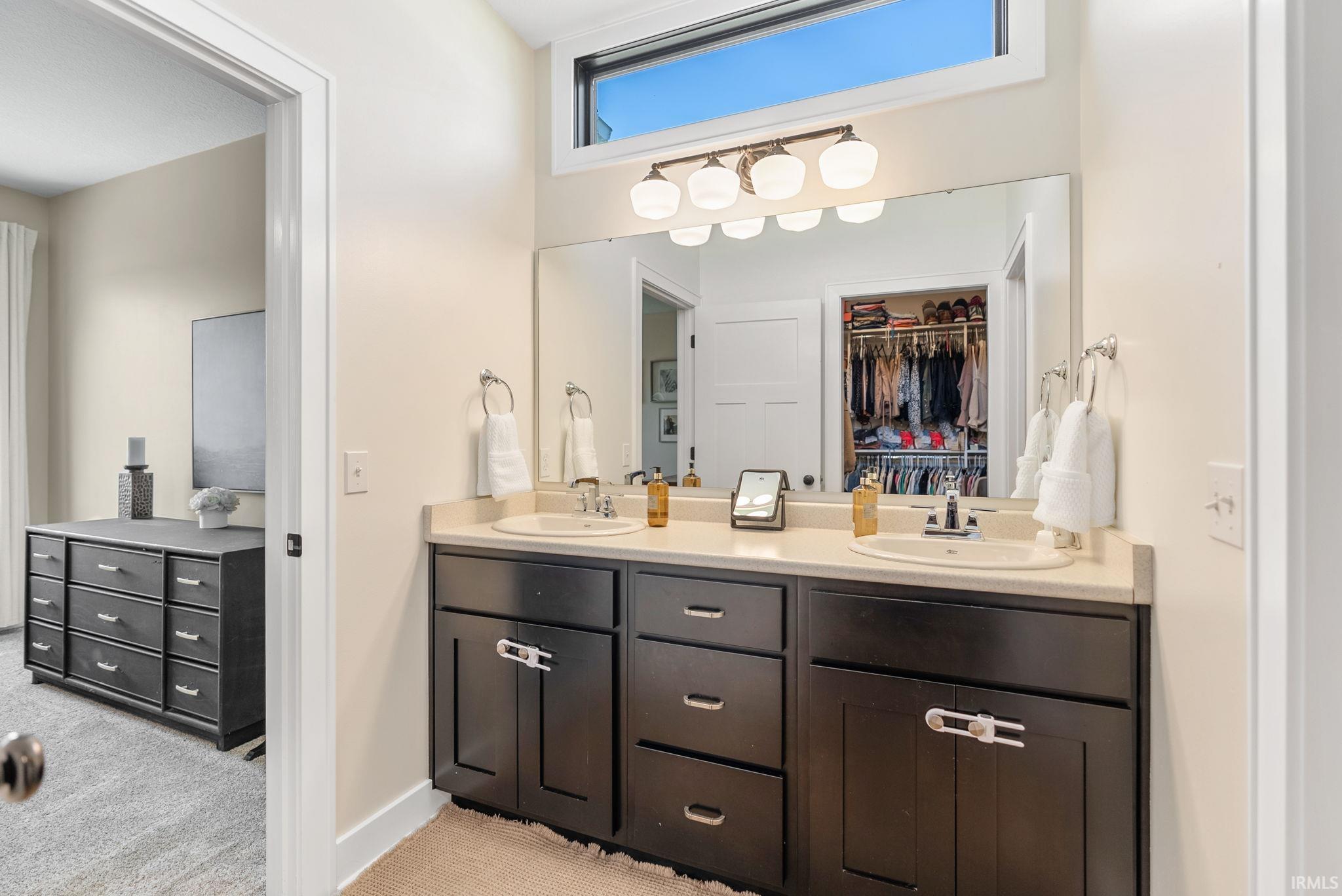 Bathroom vanity featuring dual under-mount sinks, light-toned countertop, dark wood-finish cabinetry, and a full-width mirror