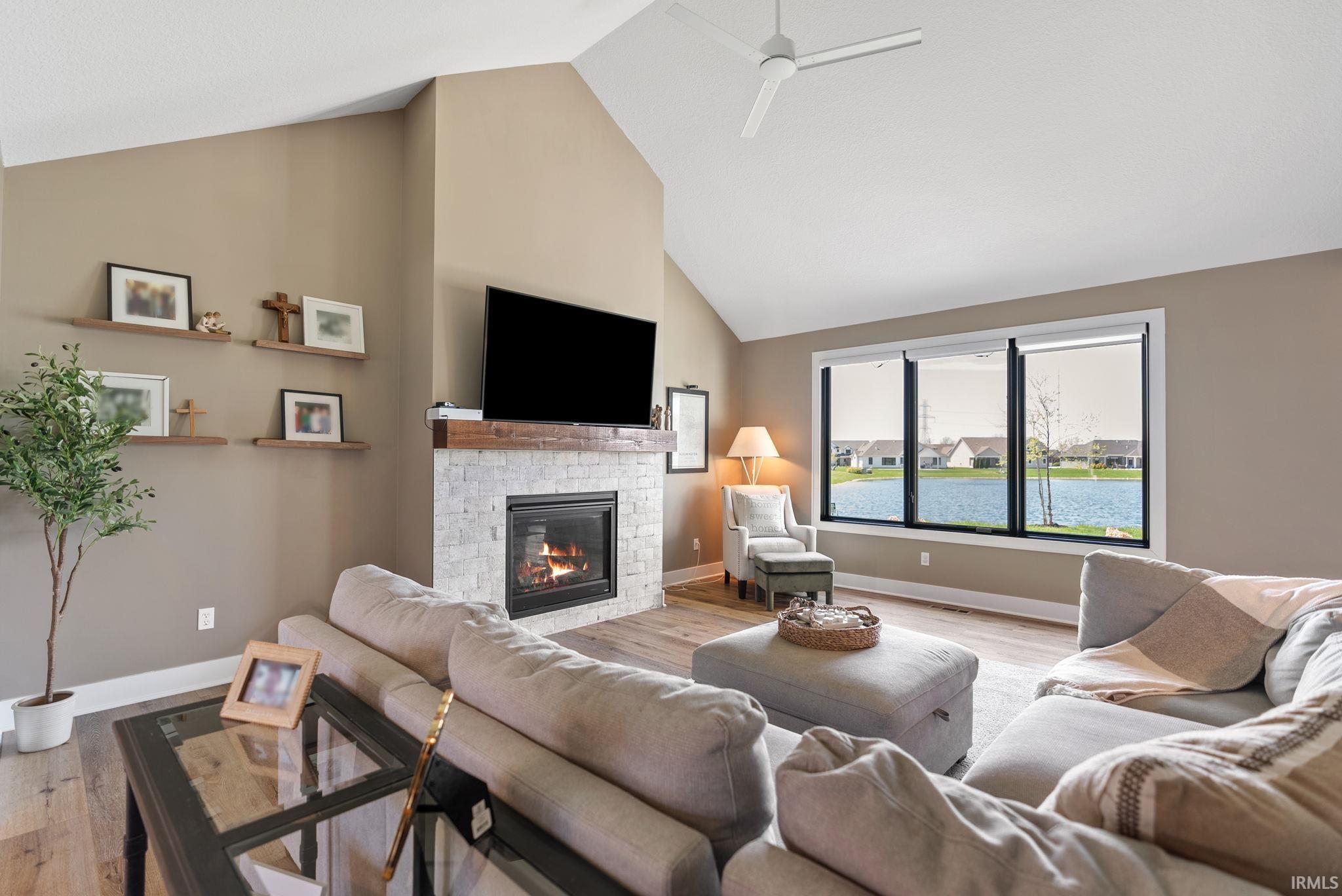 Living area with vaulted ceilings, a stacked stone fireplace with a wood mantel, and wood-finish flooring