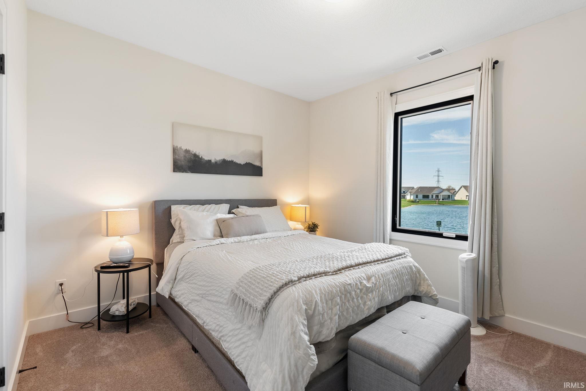 Lake-facing bedroom featuring a large picture window, neutral carpeting, and white trim molding