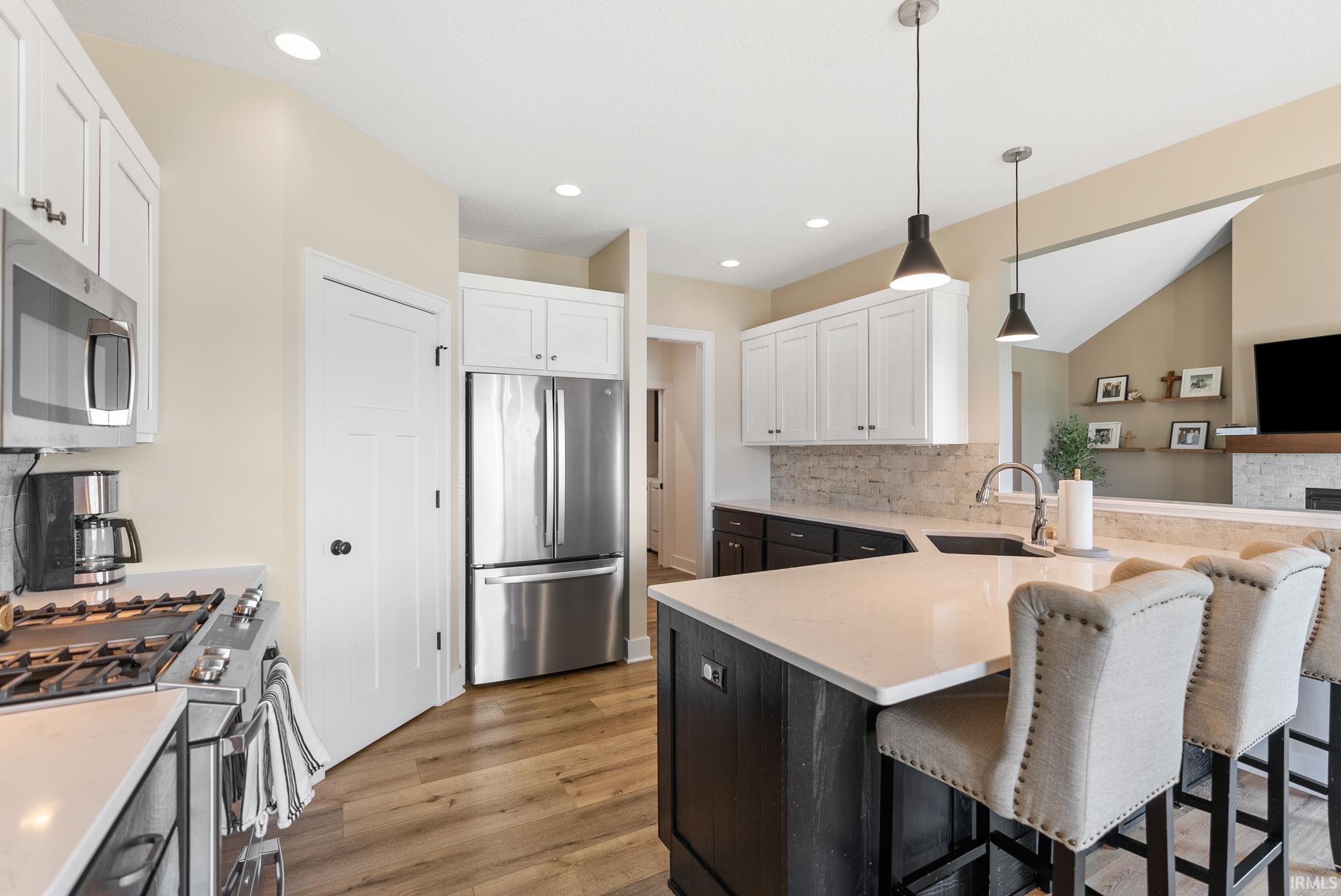 Modern kitchen featuring a large island with a light-toned countertop, stainless steel appliances, two-tone cabinetry, wood-finish flooring, and recessed lighting