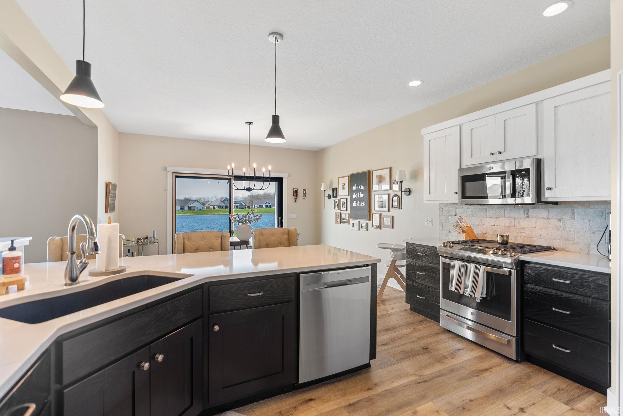 Gourmet kitchen featuring a two-tone cabinetry design, stainless steel appliances, wood-finish flooring, a white countertop island with an undermount sink, and recessed lighting