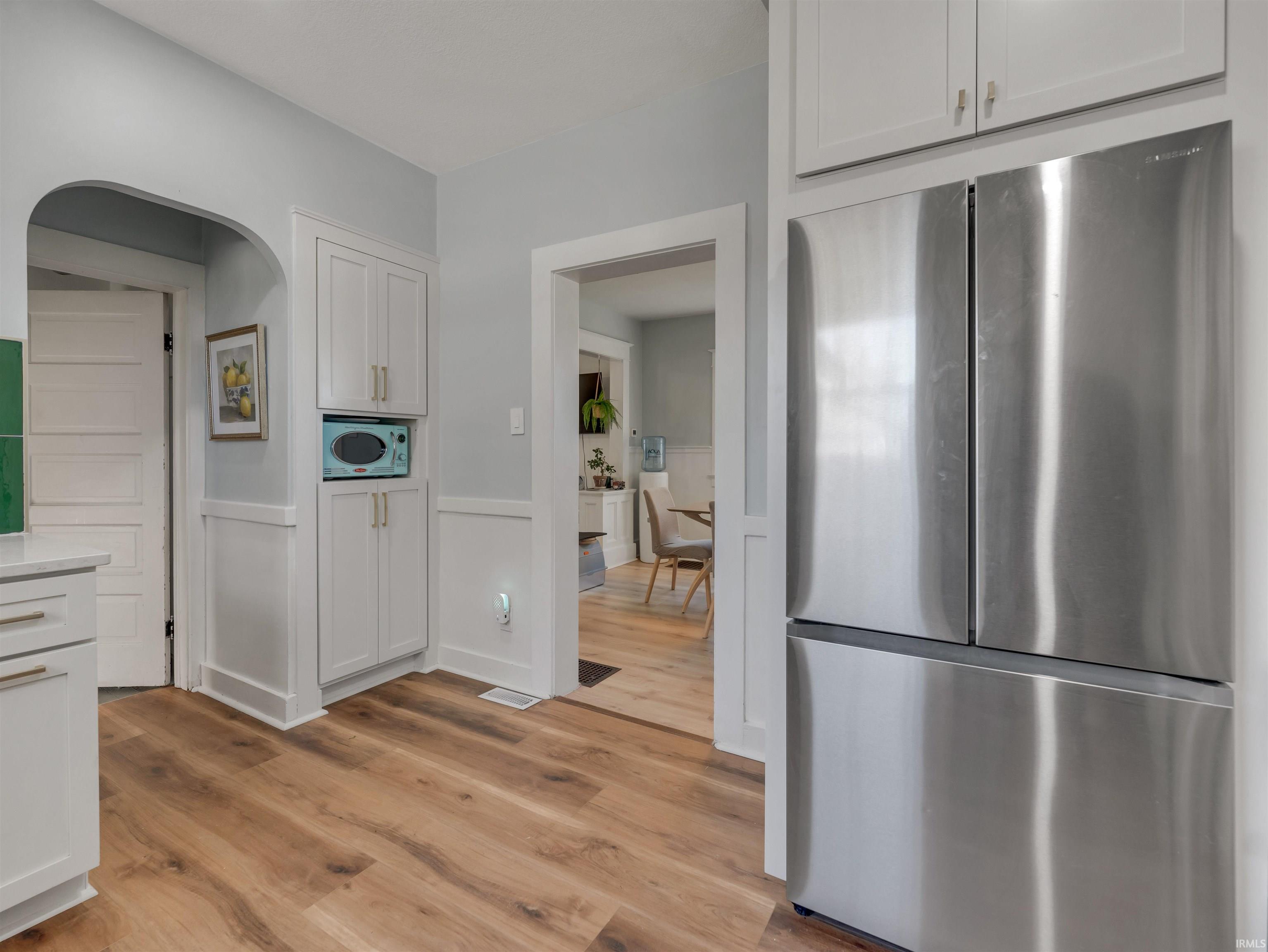 Kitchen with freestanding refrigerator, a wainscoted wall, light wood-type flooring, white cabinetry, and arched walkways