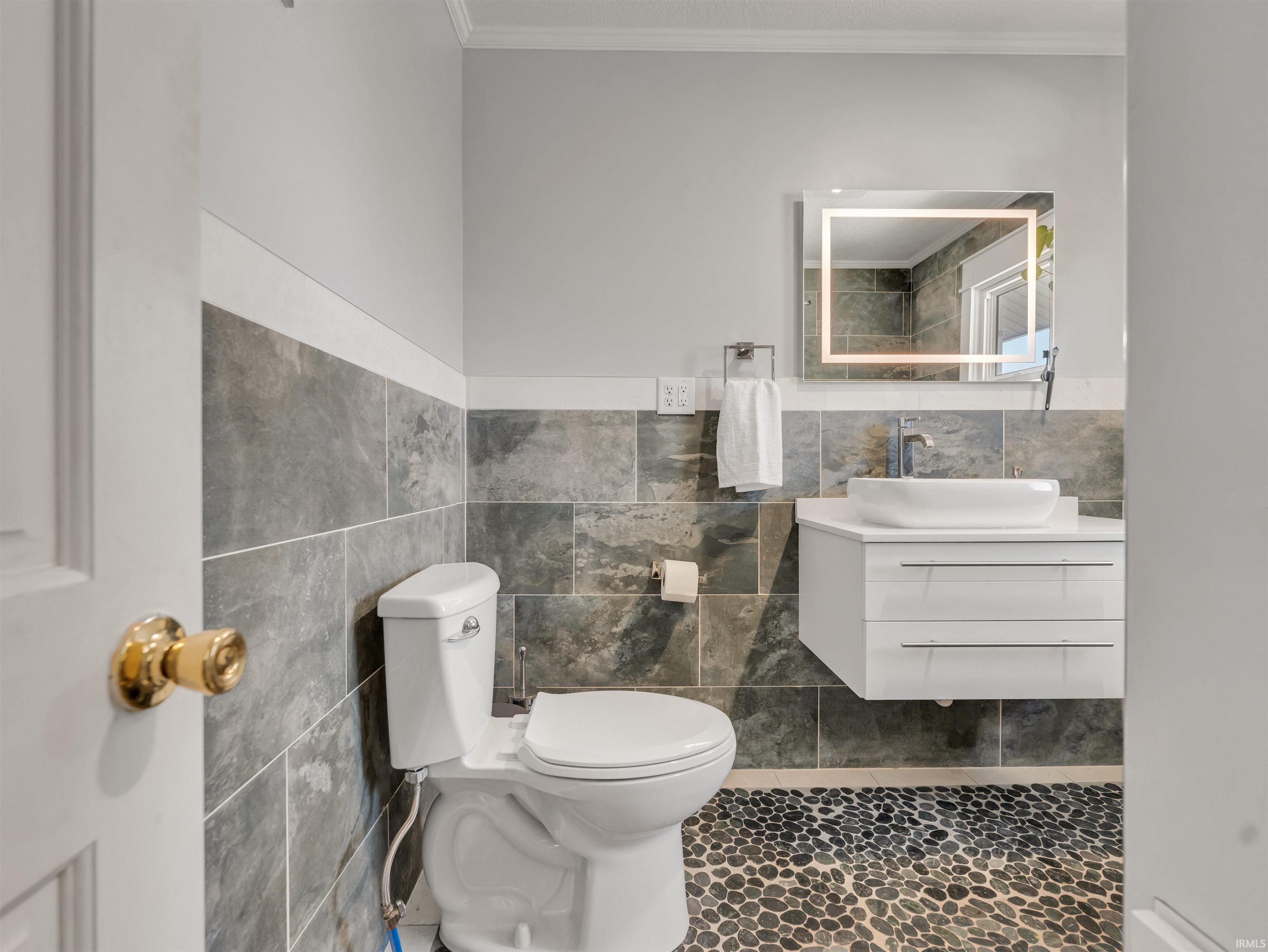Bathroom with vanity, crown molding, tile walls, and dark tile patterned flooring