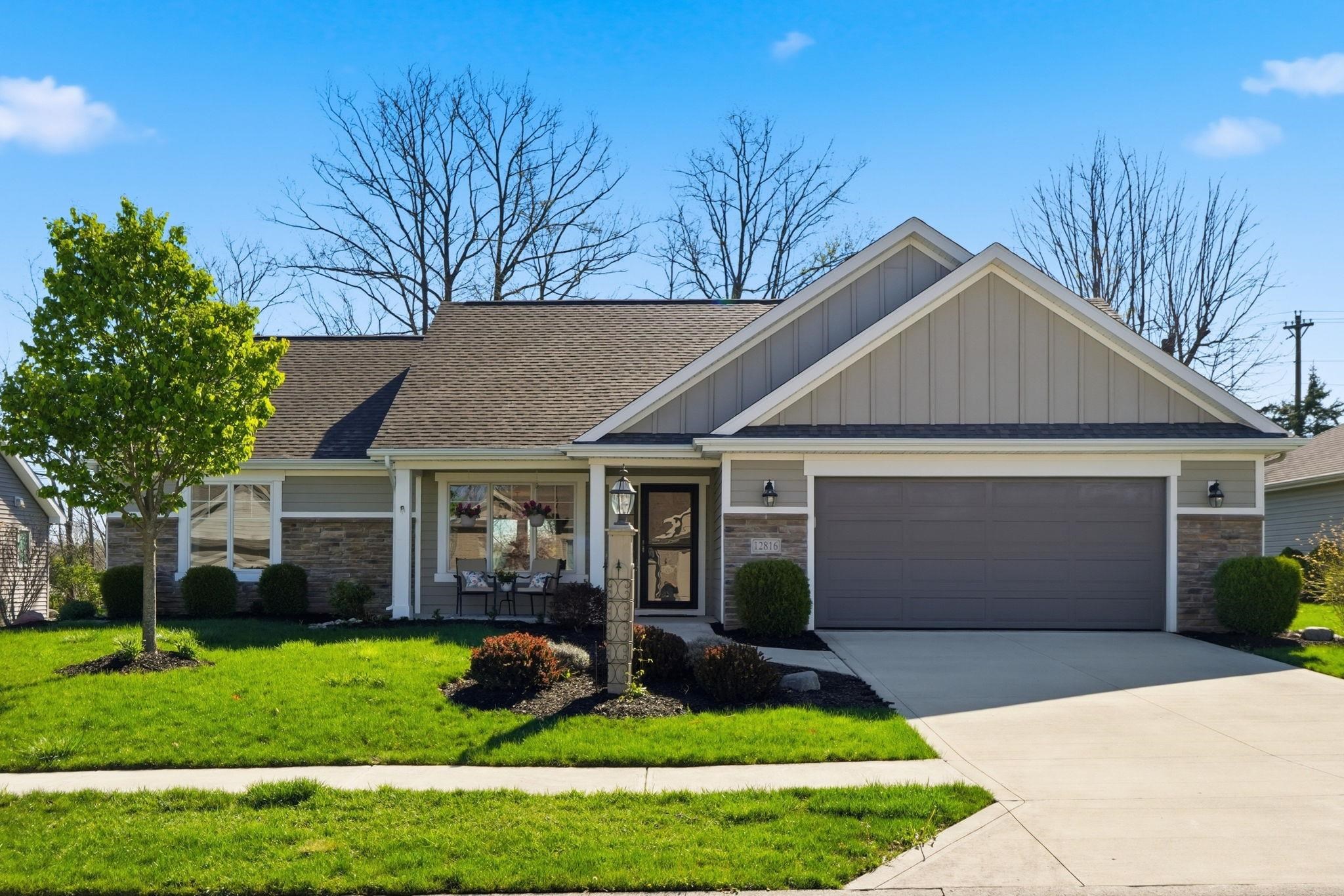 View of front of house featuring a garage, board and batten siding, driveway, a front lawn, and stone siding