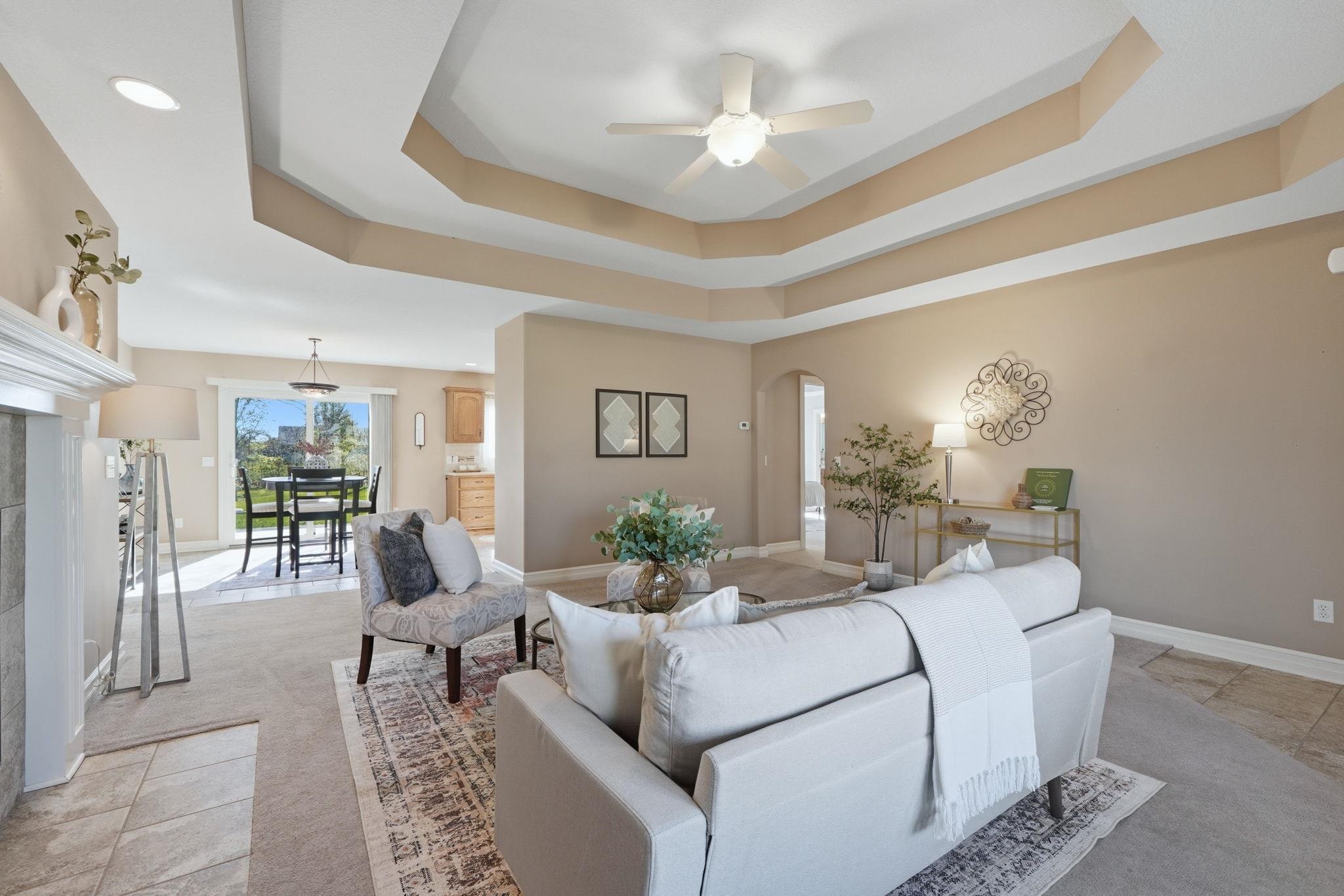 Living room featuring ceiling fan, arched walkways, light carpet, a fireplace, and light tile patterned floors
