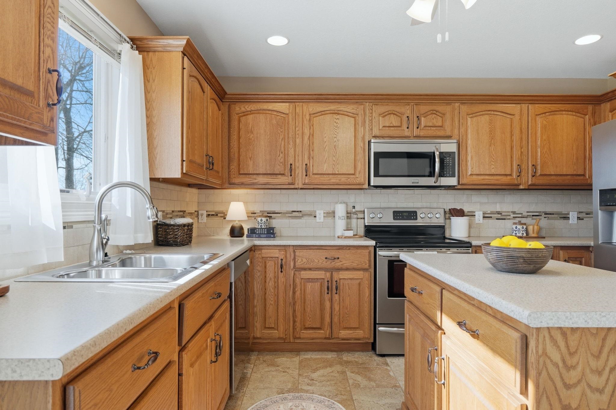 Kitchen featuring stainless steel appliances, wood finish cabinetry, light countertops, tasteful backsplash, and a ceiling fan