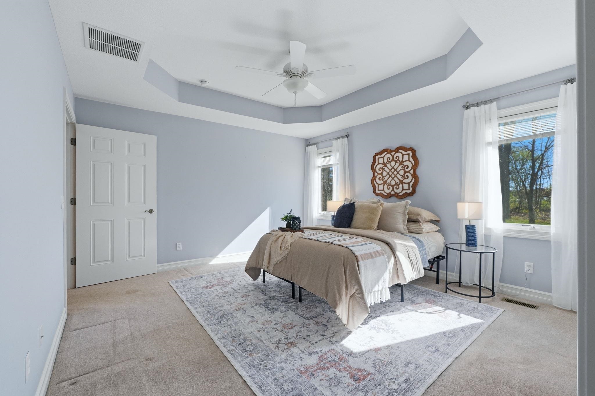 Bedroom with a tray ceiling, ceiling fan, multiple windows, and light carpet