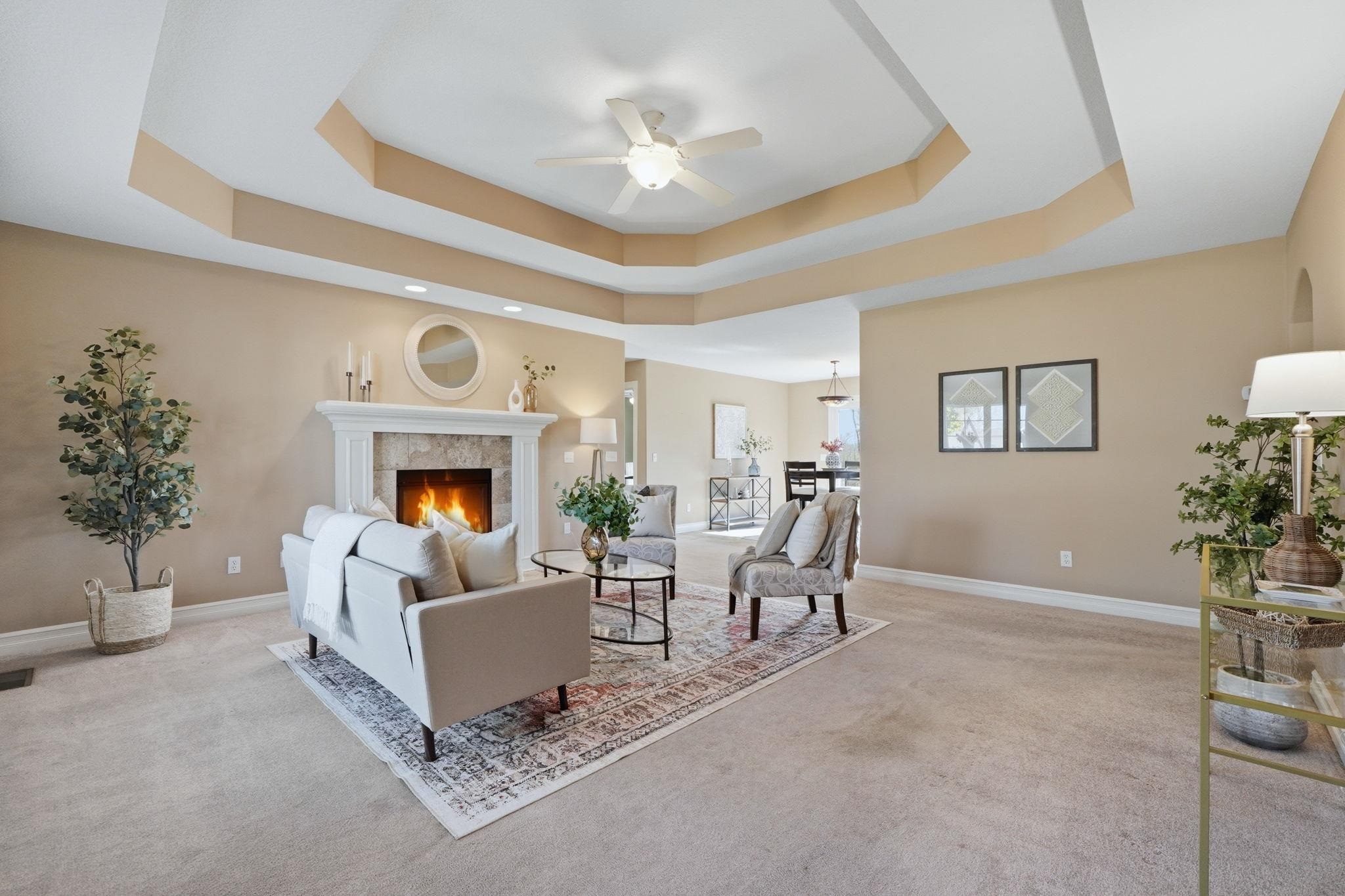 Living area with ceiling fan, a fireplace, and light carpet