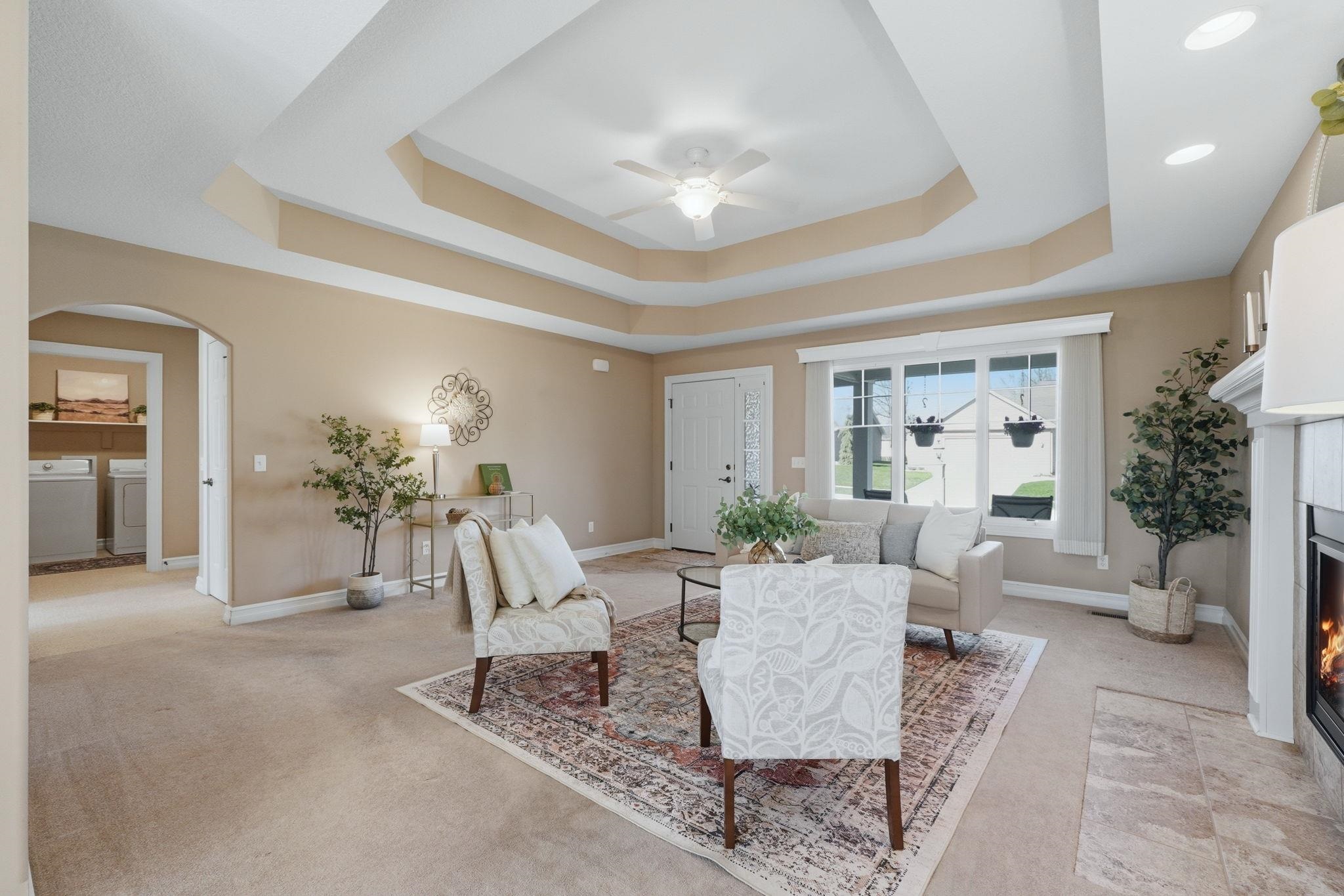 Living area with ceiling fan, a fireplace with flush hearth, light colored carpet, and arched walkways