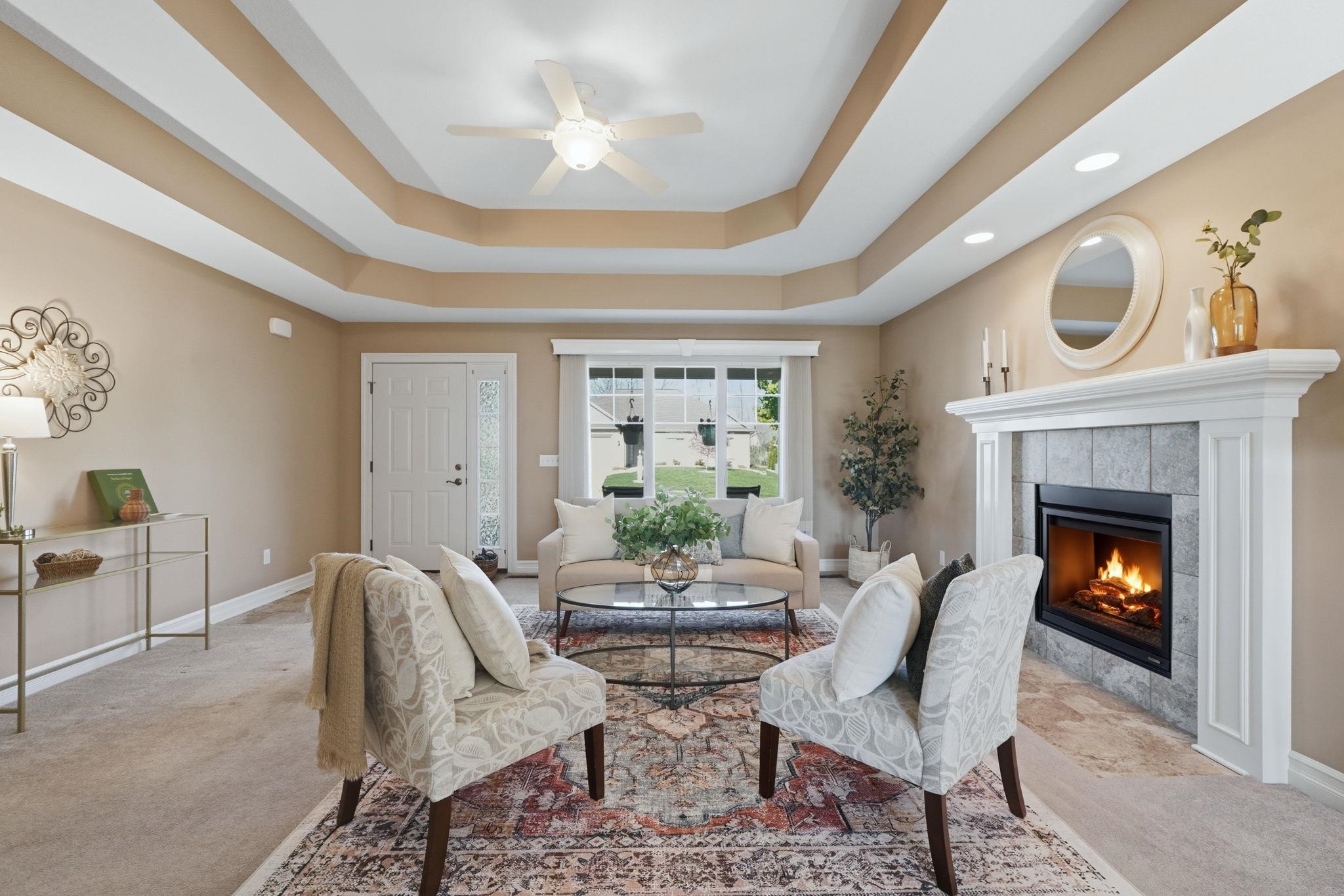 Carpeted living room with a ceiling fan, a tile fireplace, and a raised ceiling