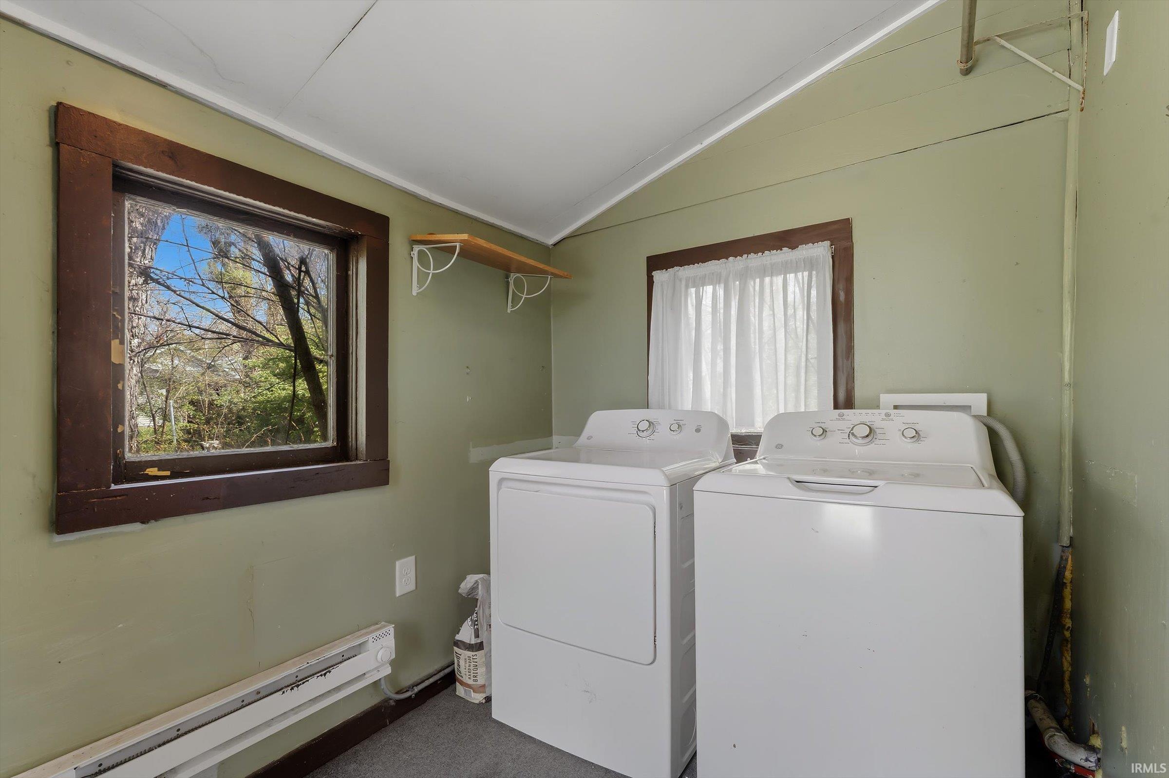Laundry room with a baseboard heating unit, washing machine and dryer, vaulted ceiling, and dark colored carpet