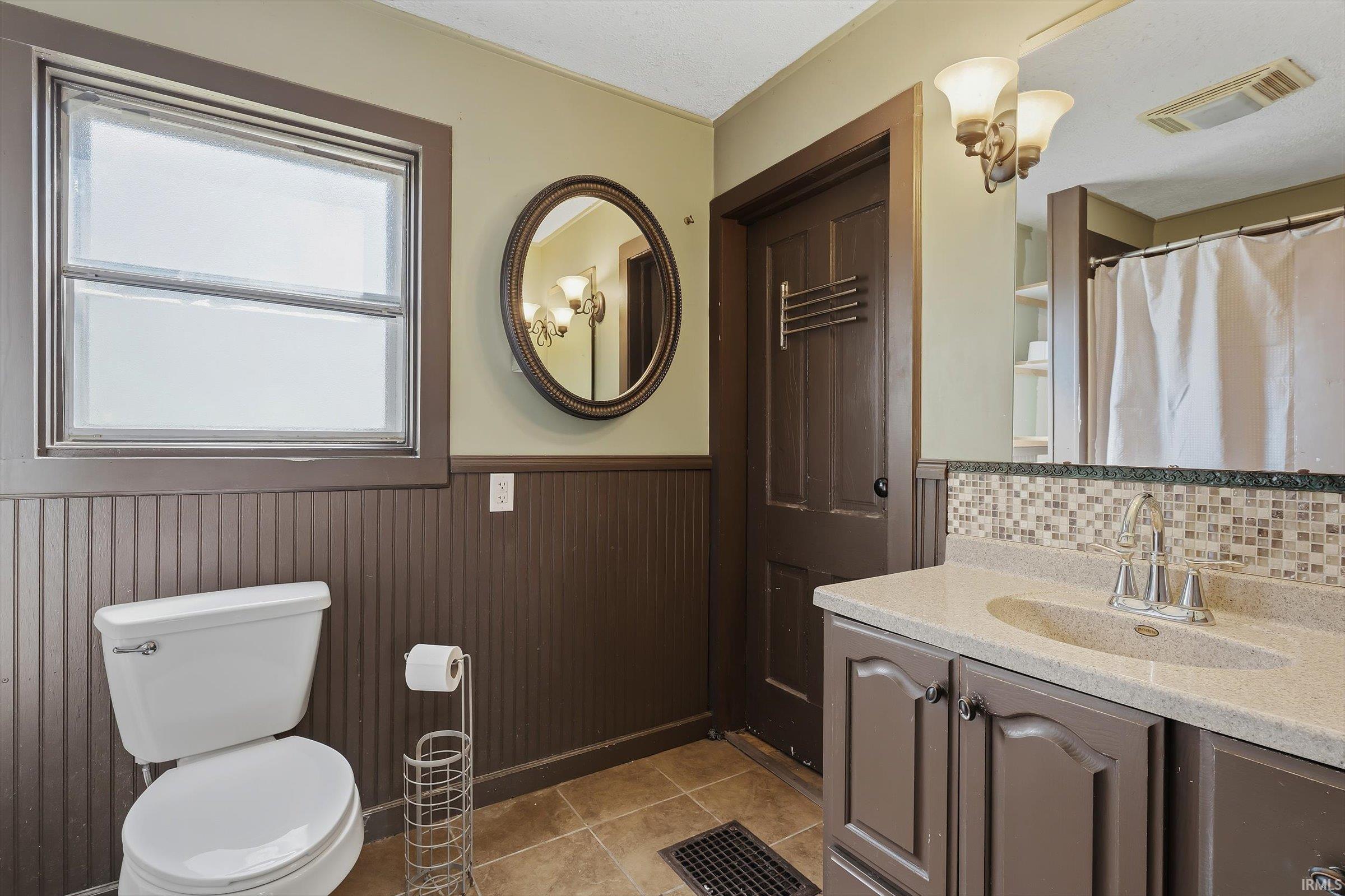 Bathroom featuring vanity, a shower with curtain, a wainscoted wall, and light tile patterned flooring