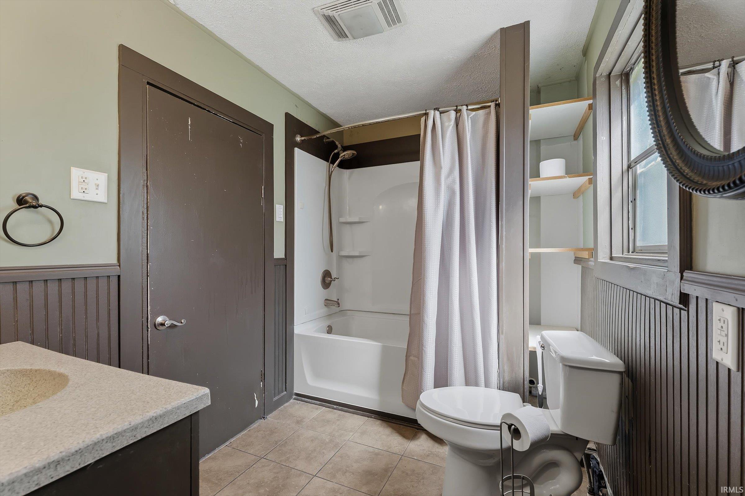 Bathroom with vanity, a wainscoted wall, shower / tub combo with curtain, light tile patterned floors, and a textured ceiling